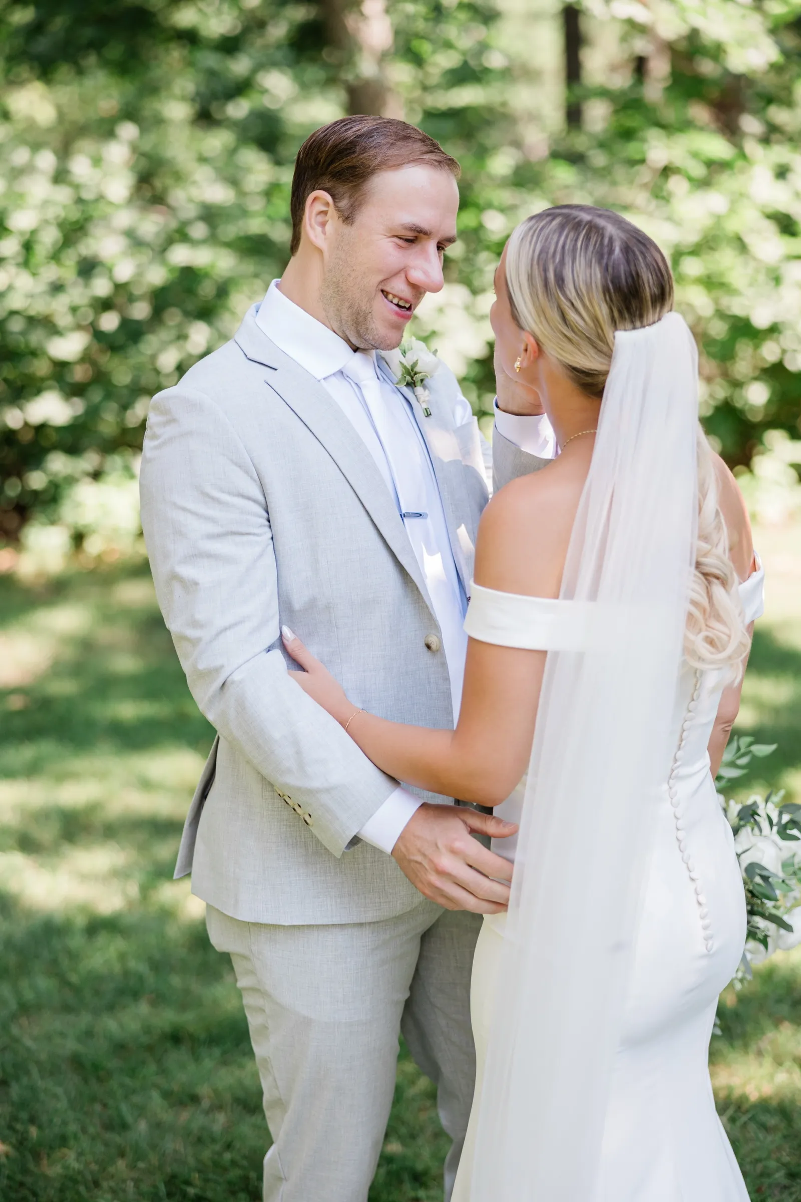 Alex smiles at Josse, her veiled back to the camera, as they hold each other on a shaded lawn — Tim Larsen Photography, Brainerd Lakes MN