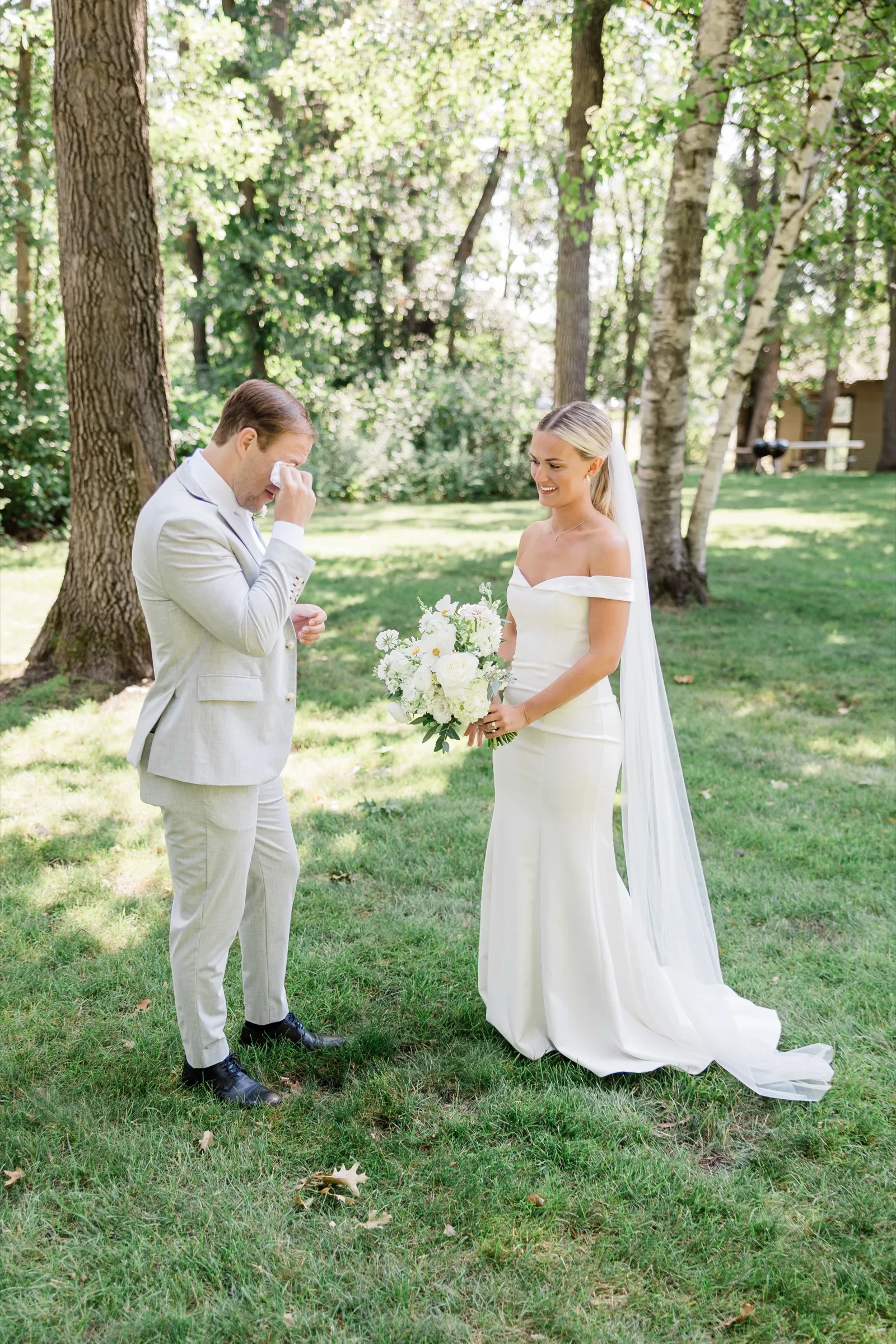 Alex wipes his eyes with a handkerchief while Josse, holding her white bouquet, smiles at him after the first look — Tim Larsen Photography, Brainerd Lakes MN