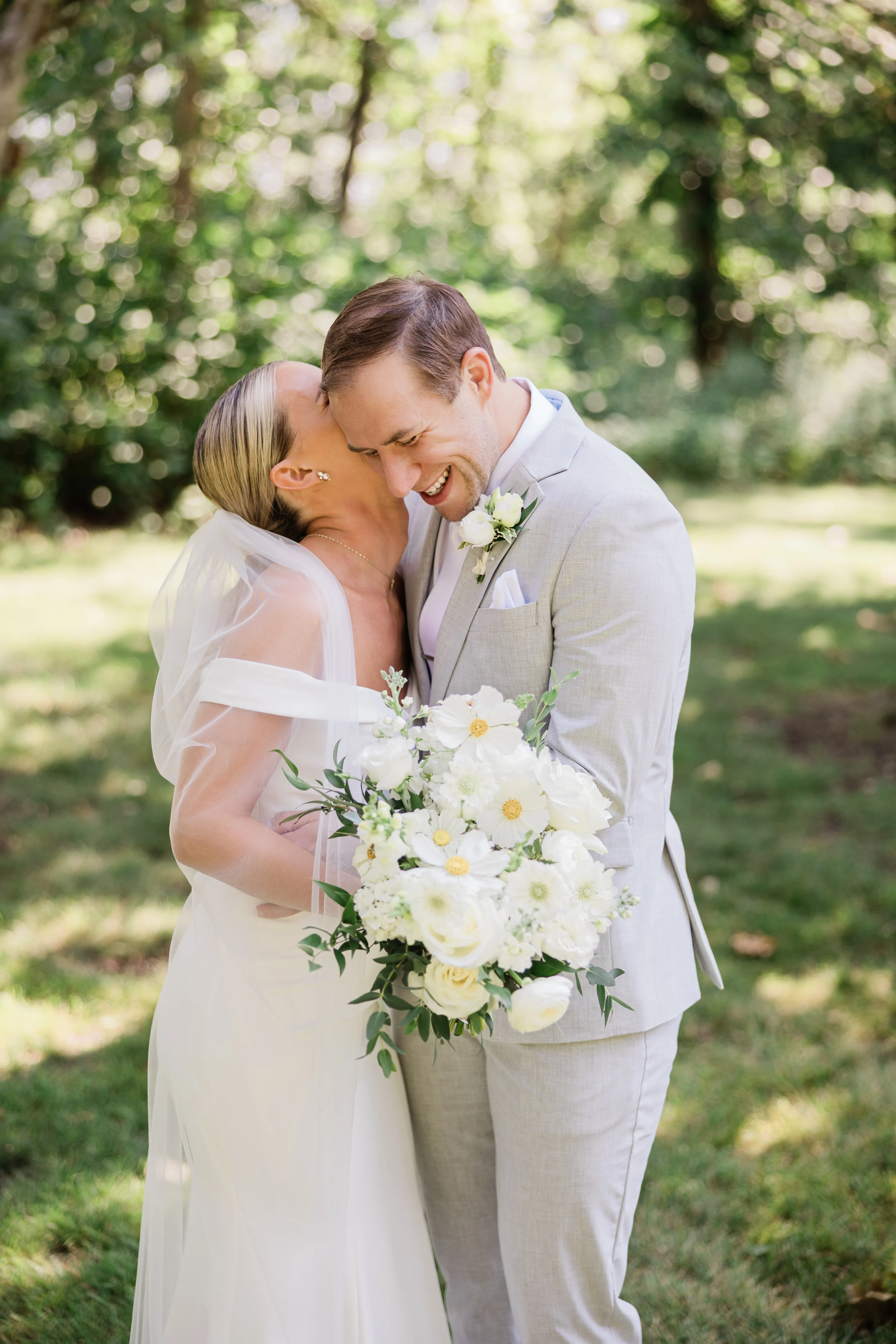 Josse and Alex hold each other close on a shaded lawn under the oaks, her veil trailing behind her — Tim Larsen Photography, Brainerd Lakes MN