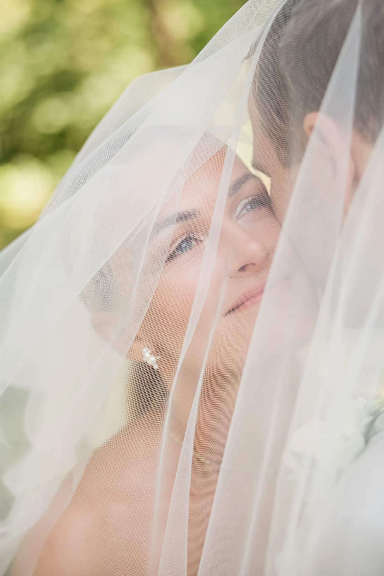 Josse gazes past the camera as she and Alex stand together beneath her sheer veil — Tim Larsen Photography, Brainerd Lakes MN