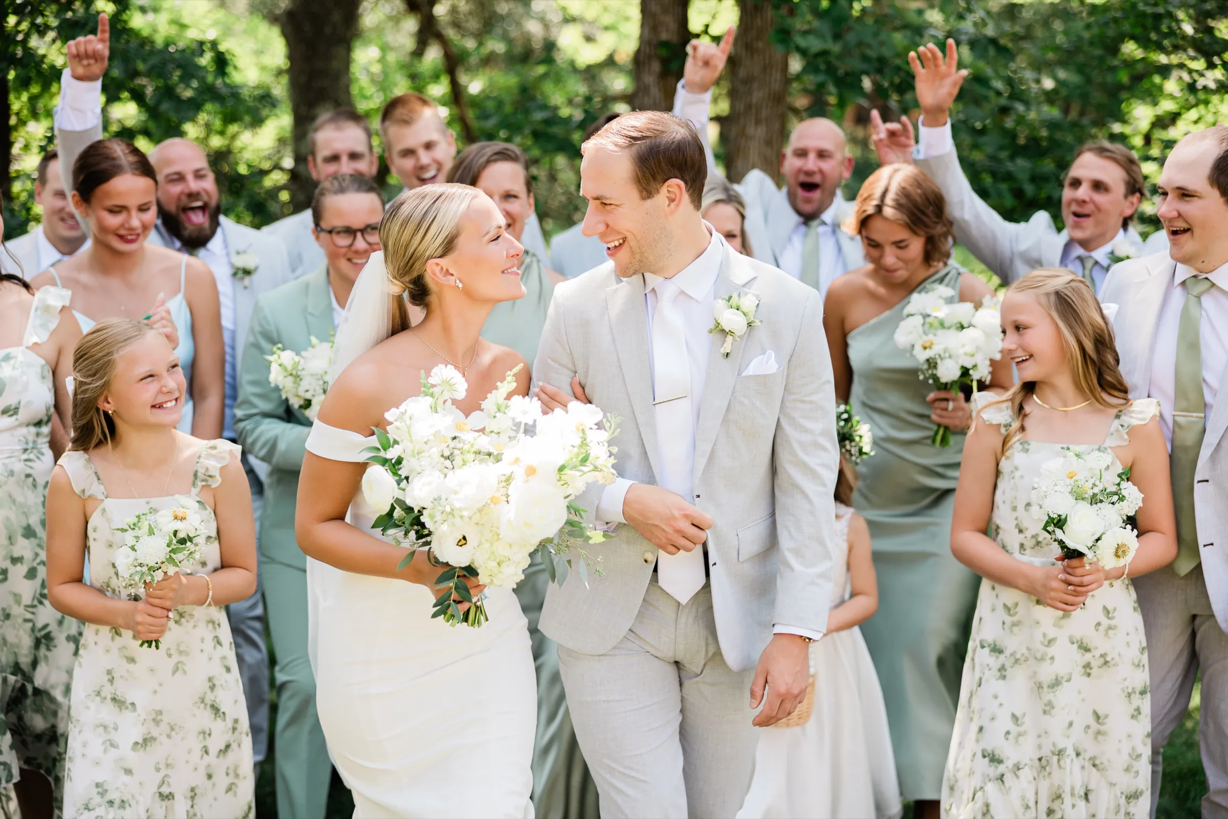 Josse and Alex walk arm in arm toward the camera, laughing, as their bridal party cheers with raised arms behind them — Tim Larsen Photography, Brainerd Lakes MN