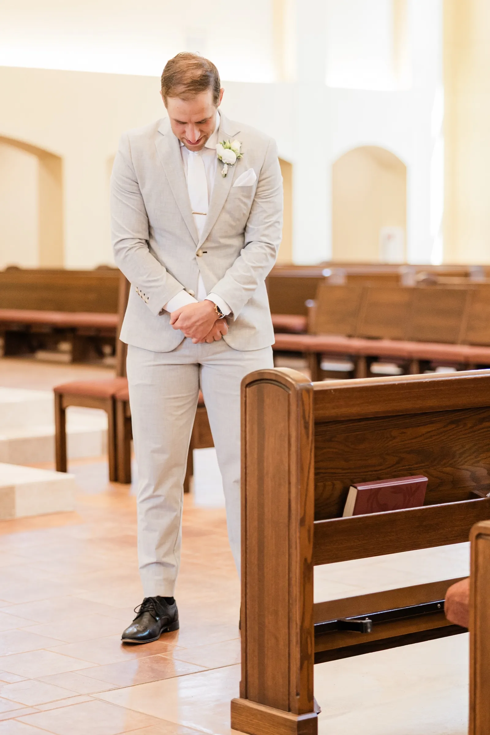 Alex stands alone in the empty church aisle before the ceremony, head bowed and hands clasped — Tim Larsen Photography, Brainerd Lakes MN