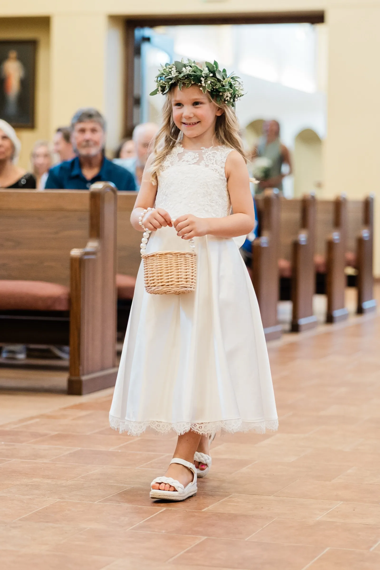 A flower girl in a greenery crown carries a woven basket down the tiled aisle of Immaculate Heart Catholic Church — Tim Larsen Photography, Brainerd Lakes MN