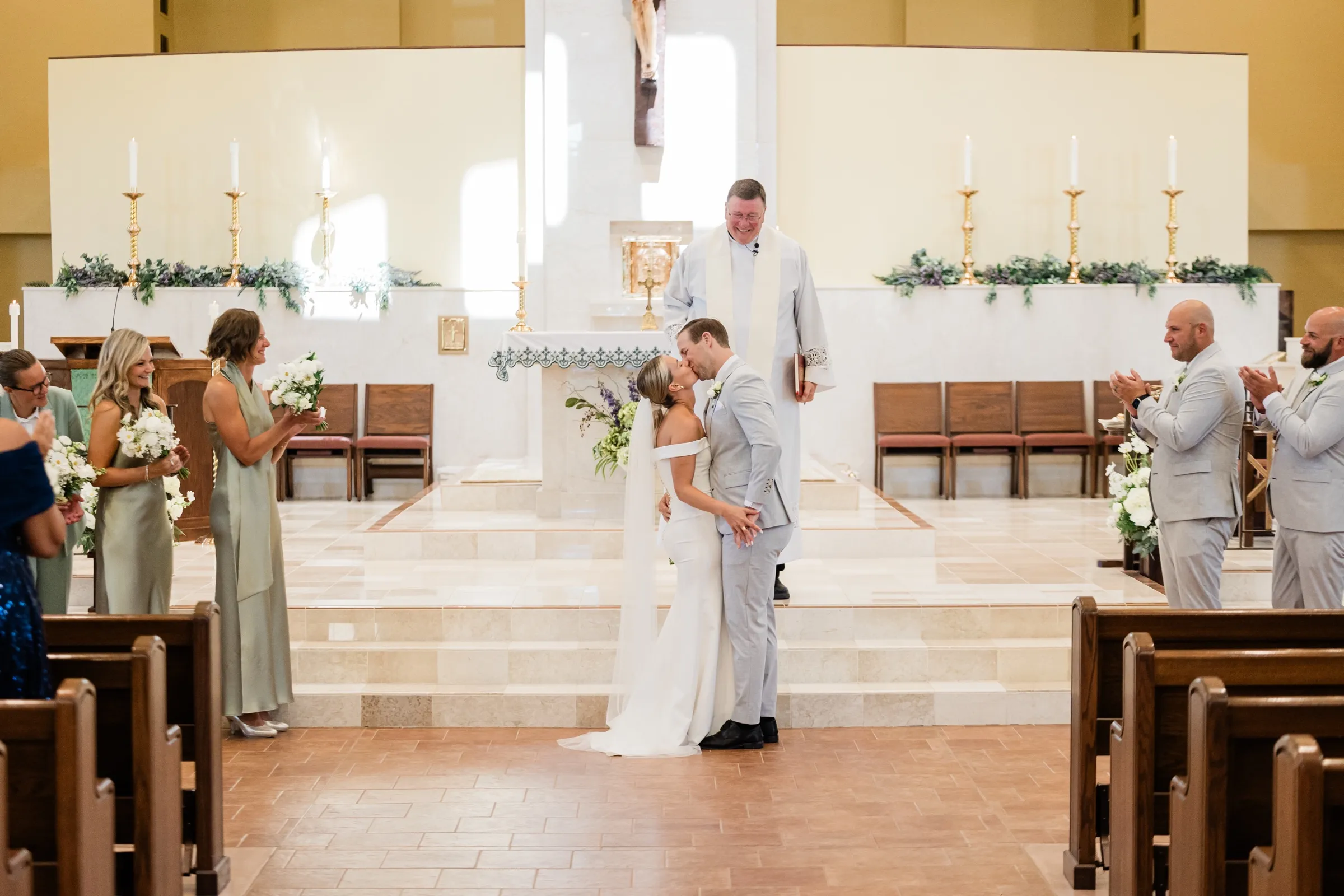 Josse and Alex share their first kiss on the altar steps as the officiant smiles and the bridal party applauds — Tim Larsen Photography, Brainerd Lakes MN