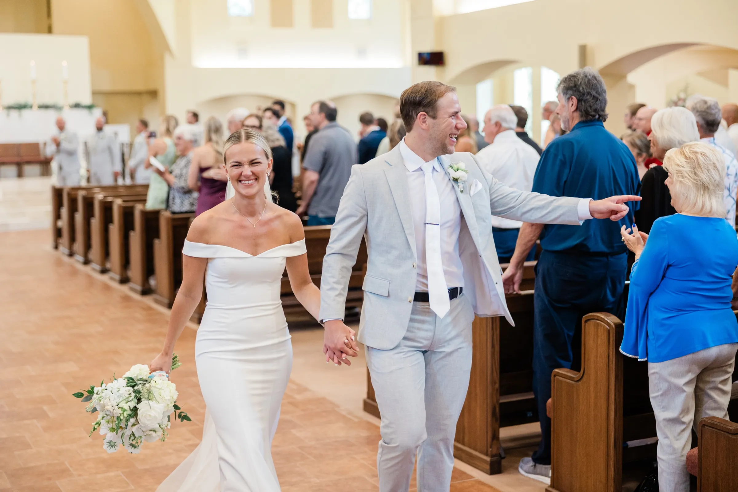 Josse laughs with her eyes squeezed shut as Alex points toward a guest while they walk hand in hand back down the aisle — Tim Larsen Photography, Brainerd Lakes MN
