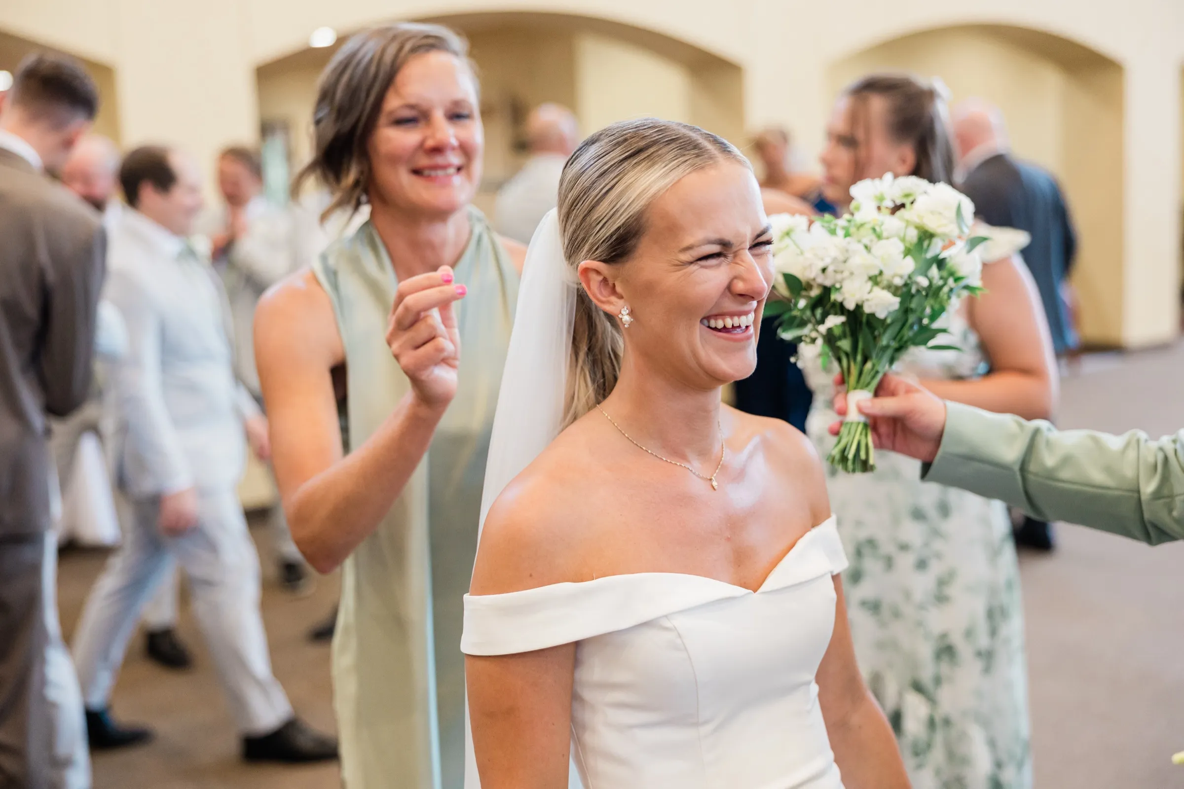 Josse laughs with her eyes squeezed shut as a bridesmaid hands her bouquet back to her in the church entryway — Tim Larsen Photography, Brainerd Lakes MN