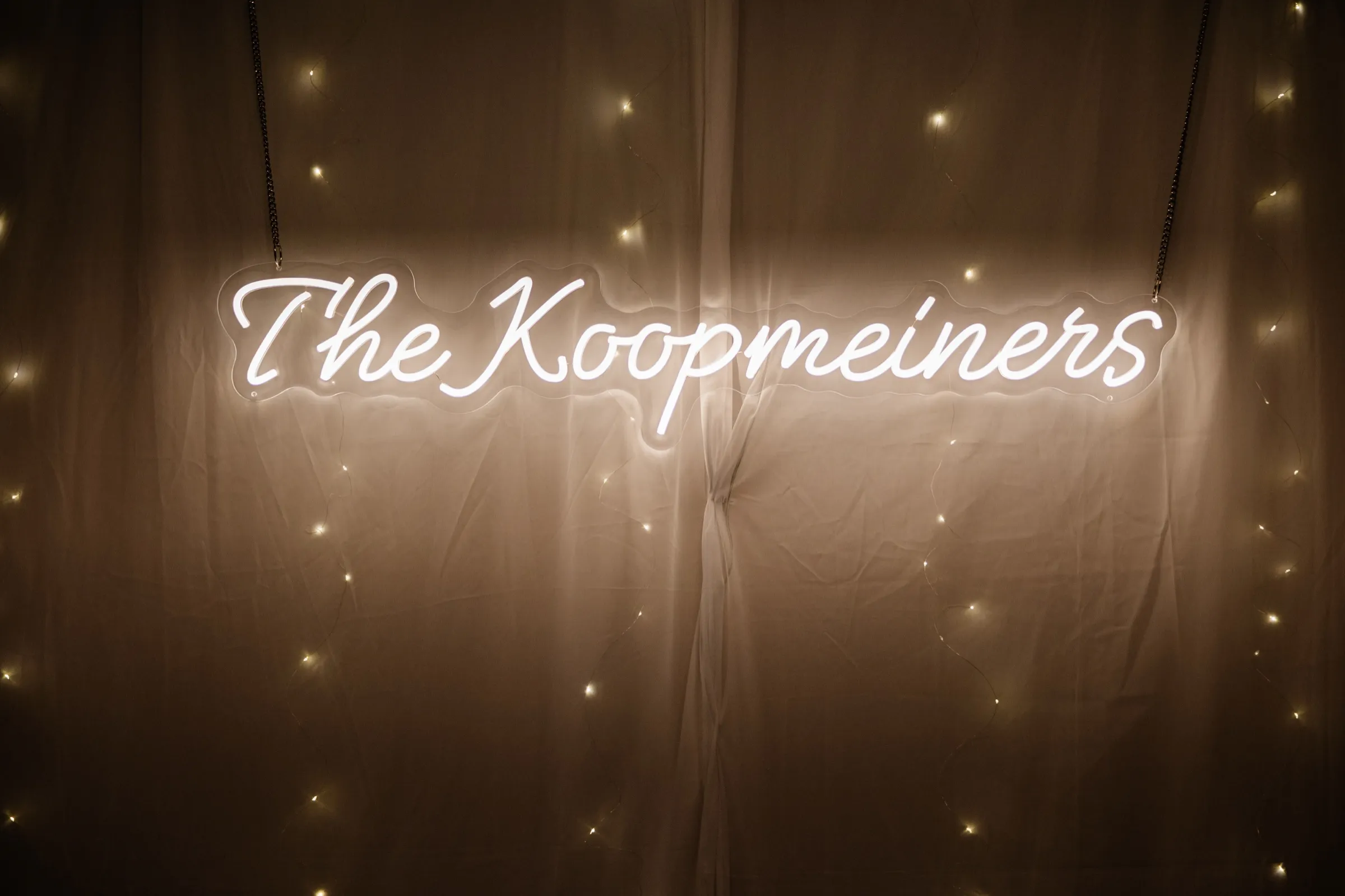 A glowing white neon sign reading 'The Koopmeiners' hangs in front of draped fabric strung with fairy lights at Whitefish Lodge — Tim Larsen Photography, Brainerd Lakes MN