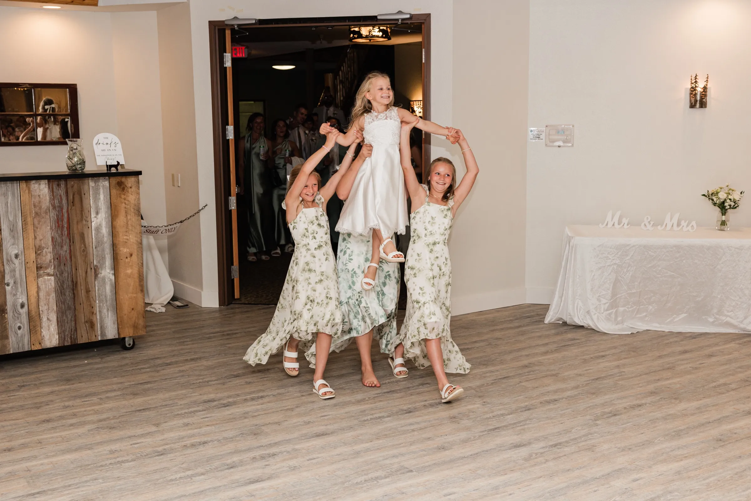 Two girls in matching floral dresses lift a third overhead as they walk onto the reception dance floor — Tim Larsen Photography, Brainerd Lakes MN