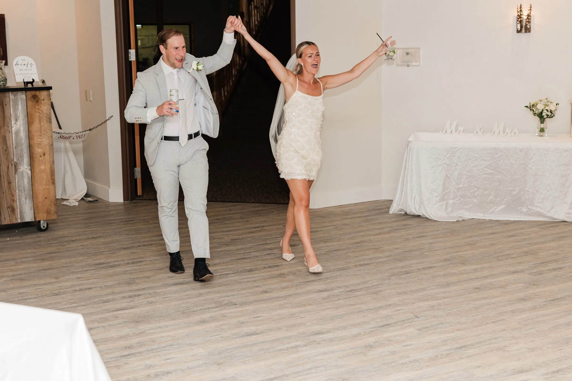 Josse and Alex walk into the Whitefish Lodge reception with hands joined and raised, an empty dance floor in front of them — Tim Larsen Photography, Brainerd Lakes MN