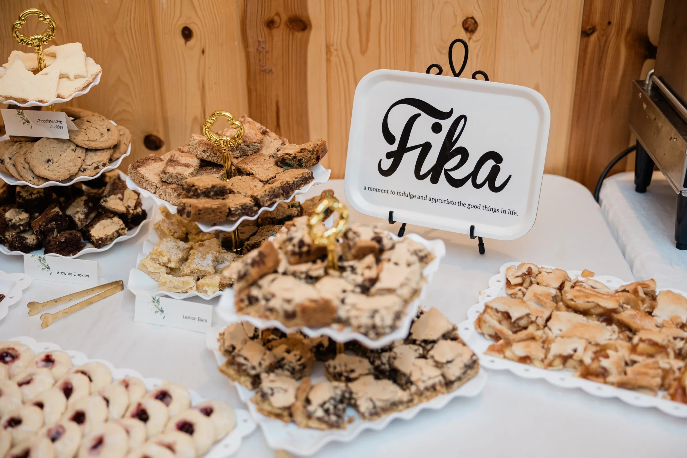 A tiered dessert table of cookies, brownie bars and lemon bars beside a hand-lettered Fika sign against the pine-paneled wall at Whitefish Lodge in Crosslake — Tim Larsen Photography, Brainerd Lakes MN