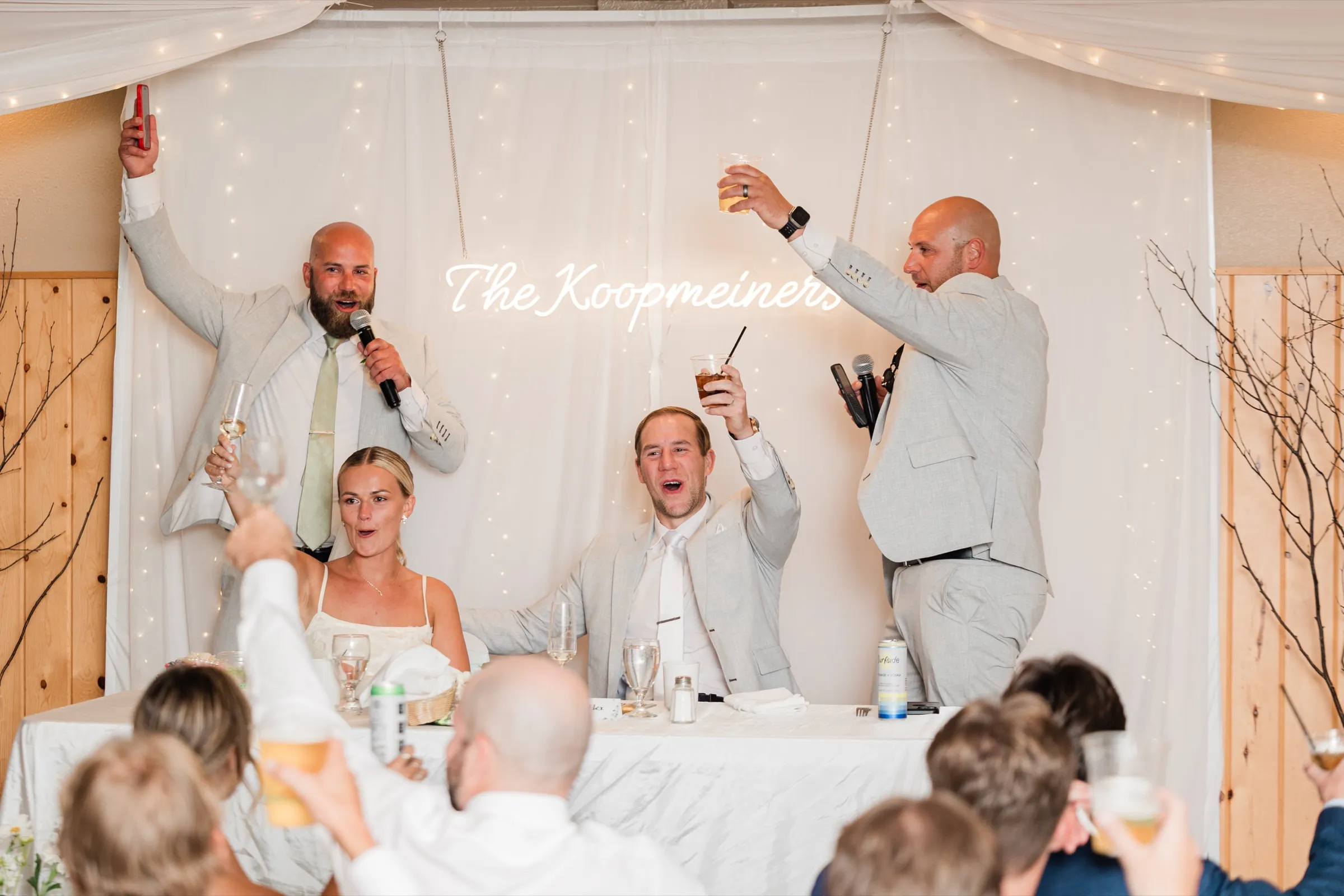 Josse and Alex cheer as two groomsmen raise drinks and a microphone during a toast at Whitefish Lodge — Tim Larsen Photography, Brainerd Lakes MN