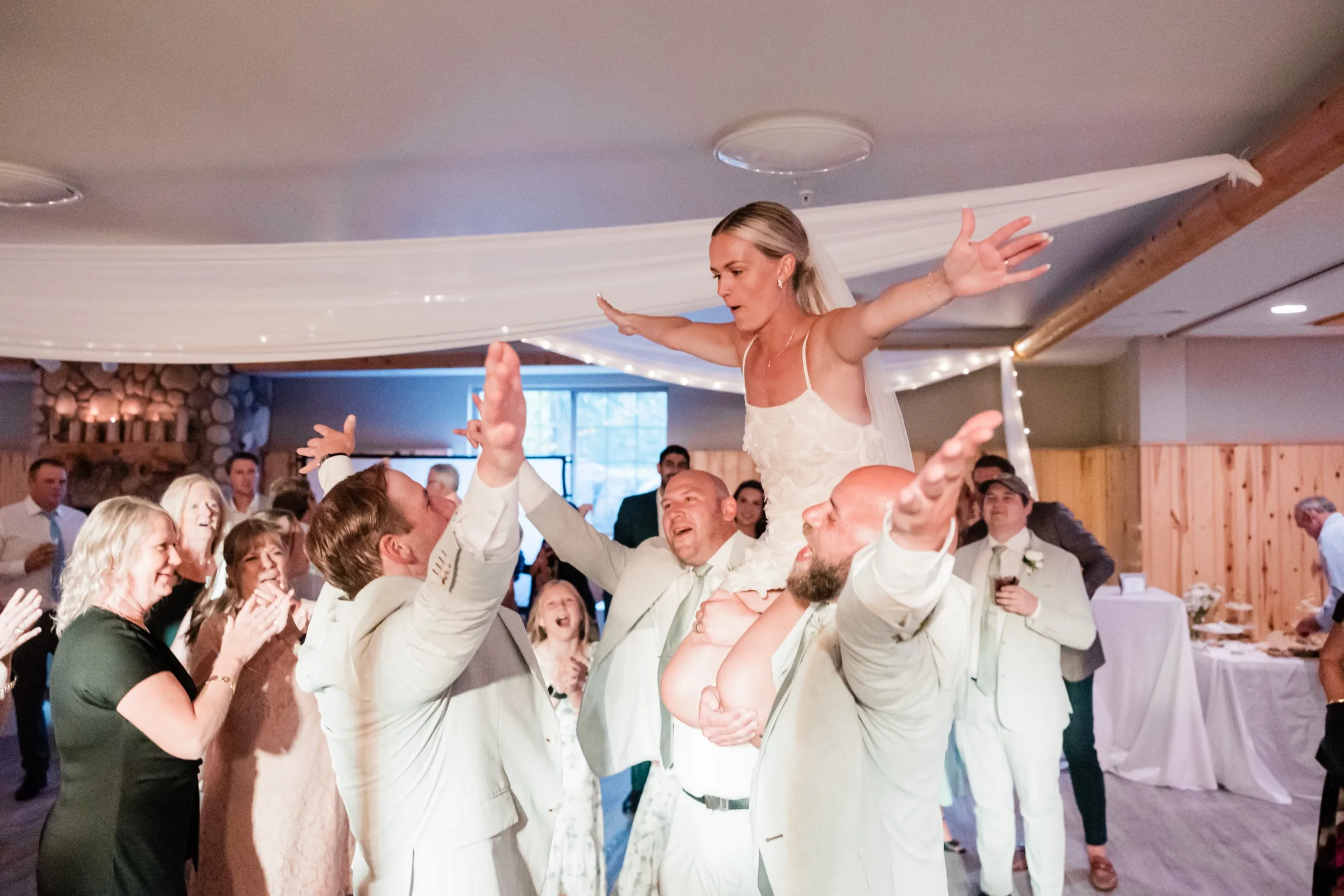 Josse is lifted overhead with her arms outstretched, surrounded by groomsmen and clapping guests on the Whitefish Lodge dance floor — Tim Larsen Photography, Brainerd Lakes MN