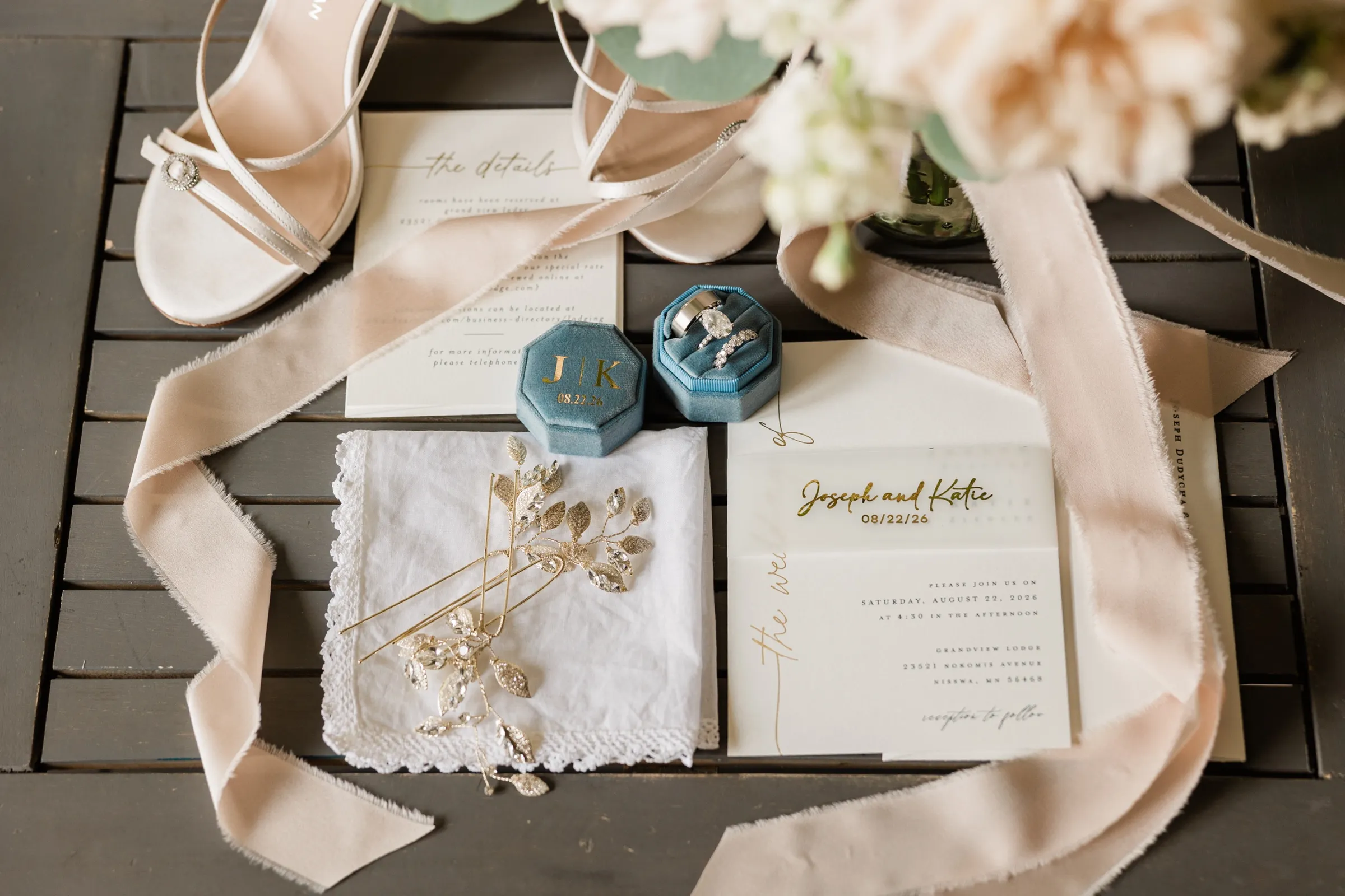 A flat-lay of the invitation suite, rings in a dusty blue velvet box, bridal heels, a gold hairpiece and blush silk ribbon on a slatted table. — Tim Larsen Photography, Brainerd Lakes MN