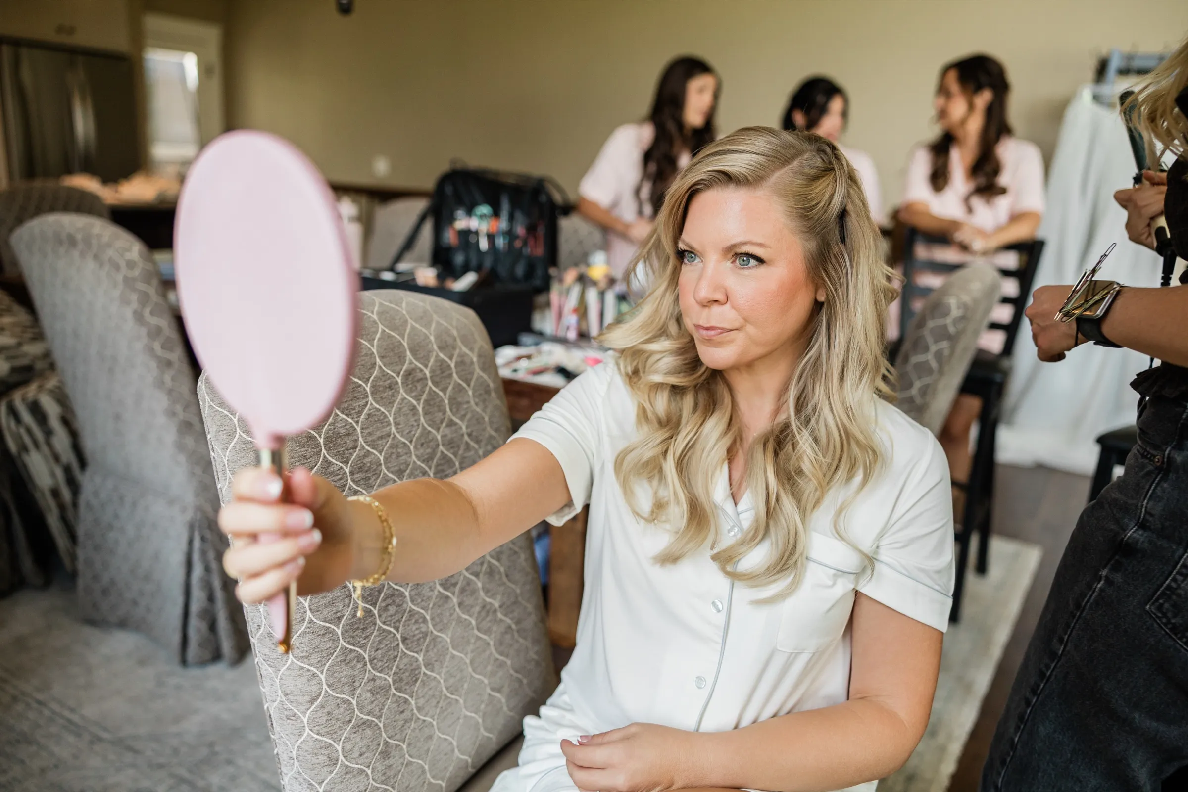 The bride holds a pink hand mirror out at arm's length and studies her reflection while her bridesmaids sit behind her. — Tim Larsen Photography, Brainerd Lakes MN