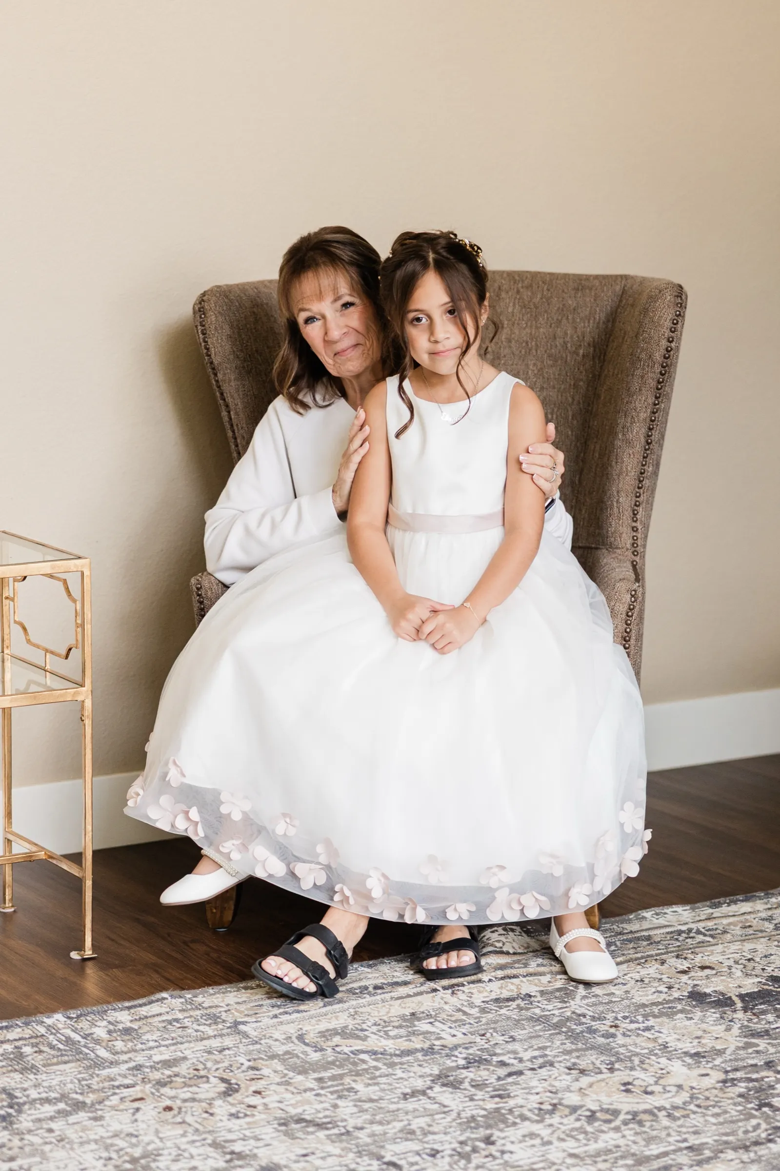 An older woman sits in a wingback chair with her arms around the flower girl, her eyes wet as she looks at the camera. — Tim Larsen Photography, Brainerd Lakes MN