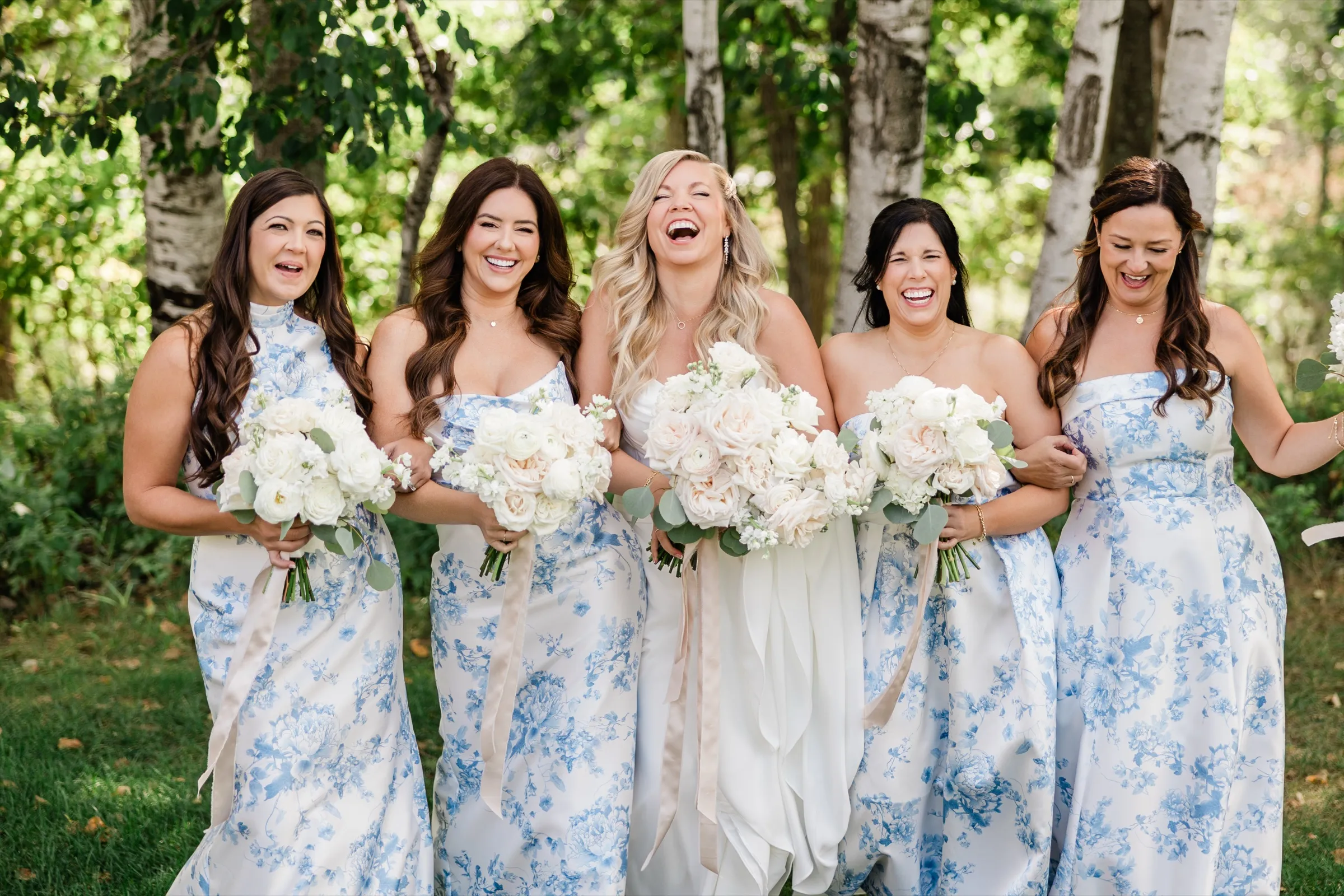 The bride laughs with her head back while all four bridesmaids laugh alongside her, arms linked, walking through a birch grove. — Tim Larsen Photography, Brainerd Lakes MN