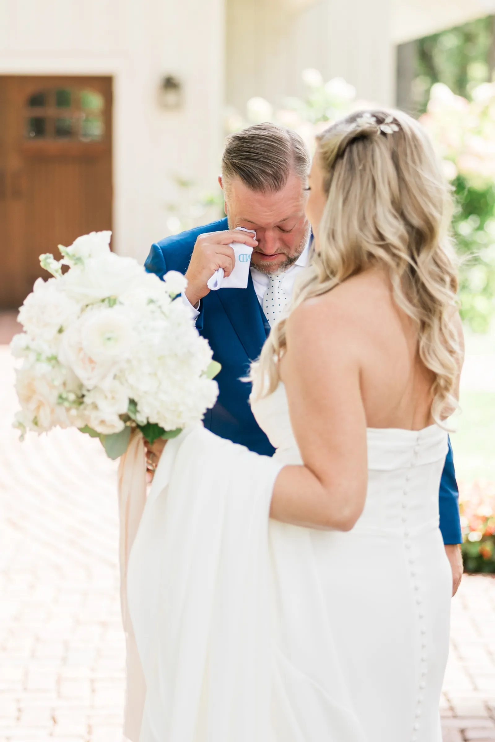 The groom pauses with a hand to his face during the first look while the bride stands facing him with her bouquet on the brick path outside the Chapel. — Tim Larsen Photography, Brainerd Lakes MN
