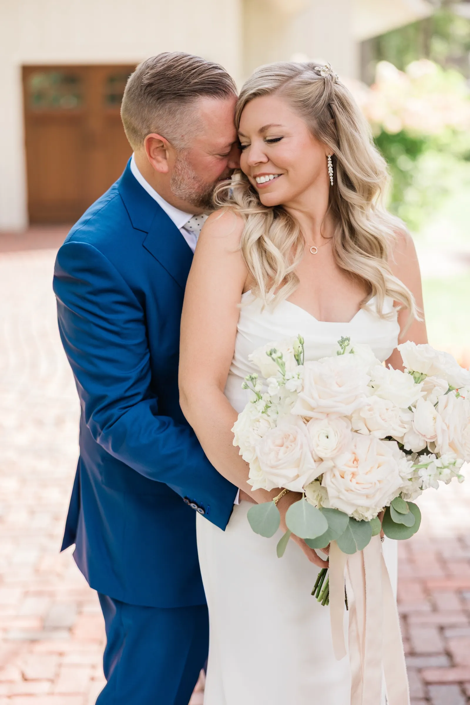 The groom leans into the bride's shoulder from behind with his eyes closed while she smiles with her eyes shut, holding her bouquet. — Tim Larsen Photography, Brainerd Lakes MN