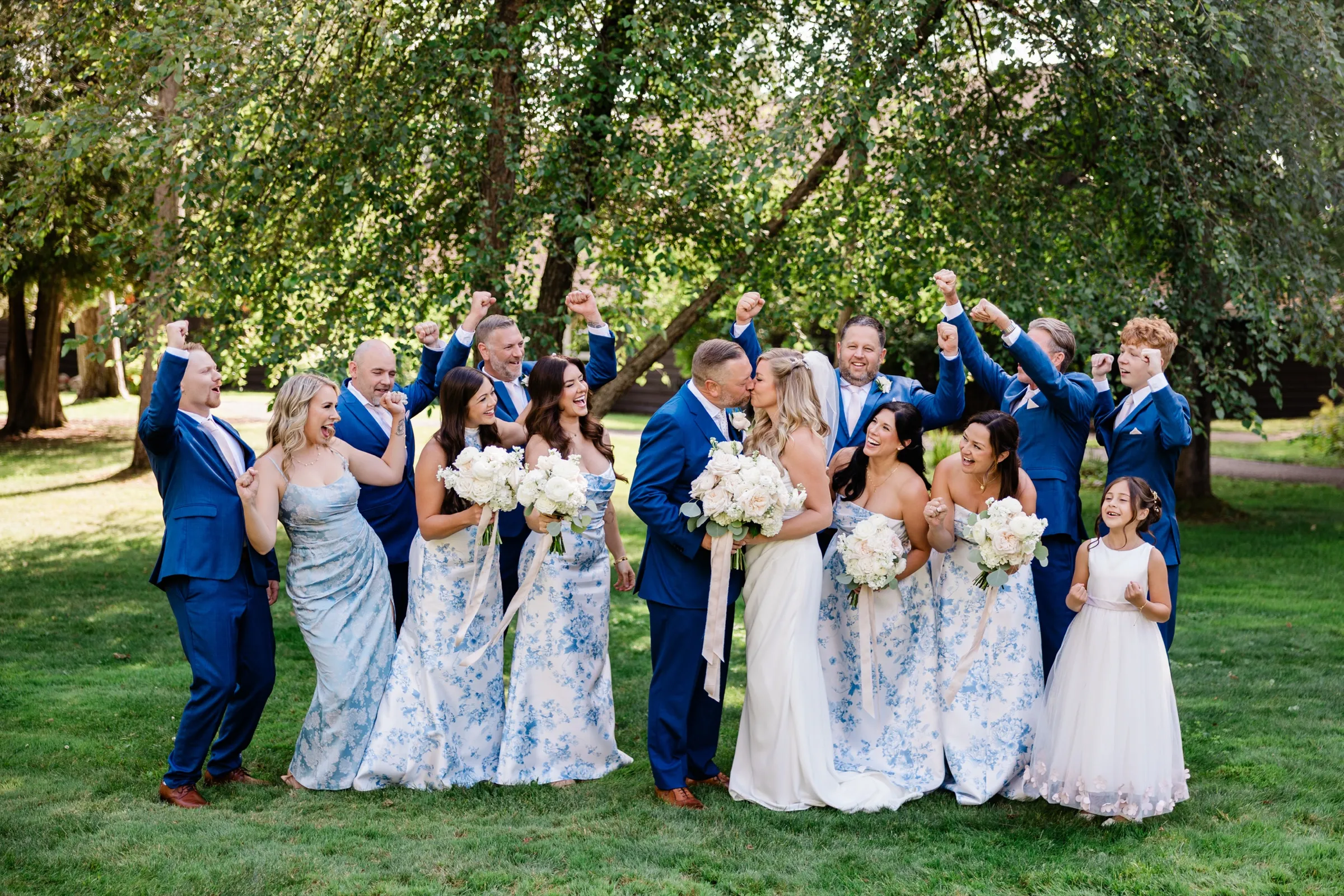 The couple kiss at the center of their wedding party while the attendants throw their fists in the air and cheer. — Tim Larsen Photography, Brainerd Lakes MN