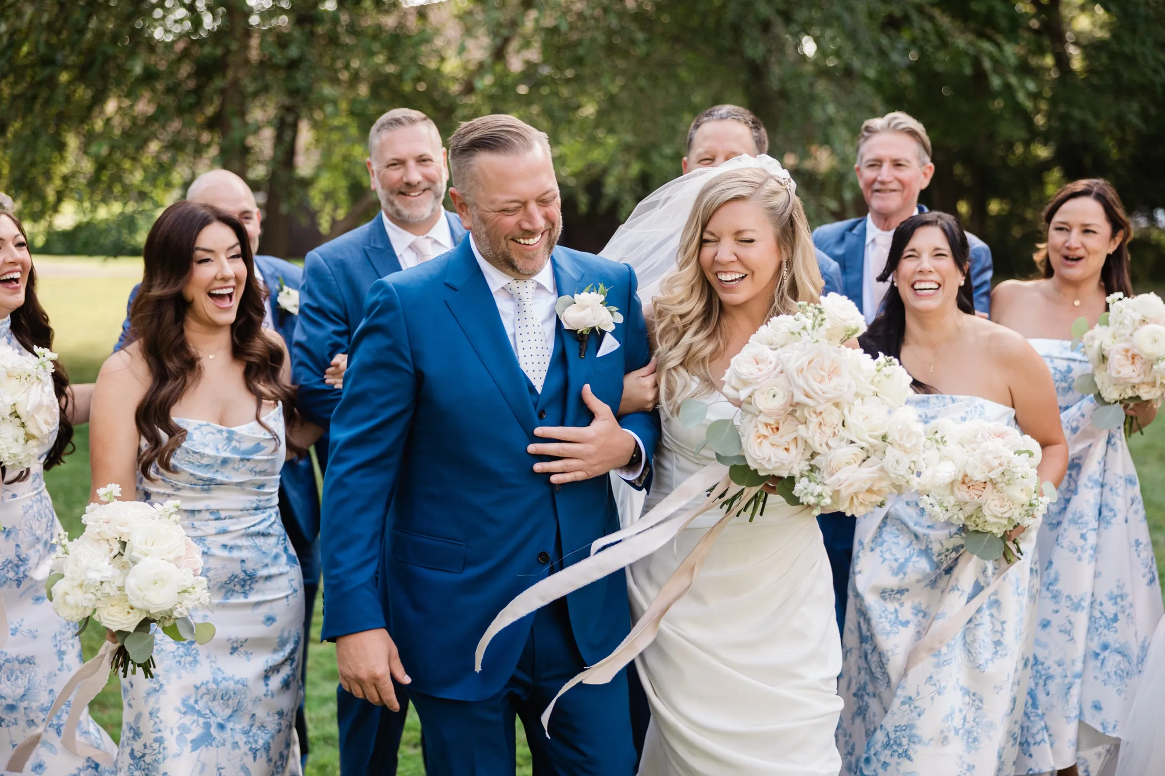 The bride and groom walk toward the camera laughing with their eyes closed, her veil lifting behind her and the wedding party laughing on either side. — Tim Larsen Photography, Brainerd Lakes MN