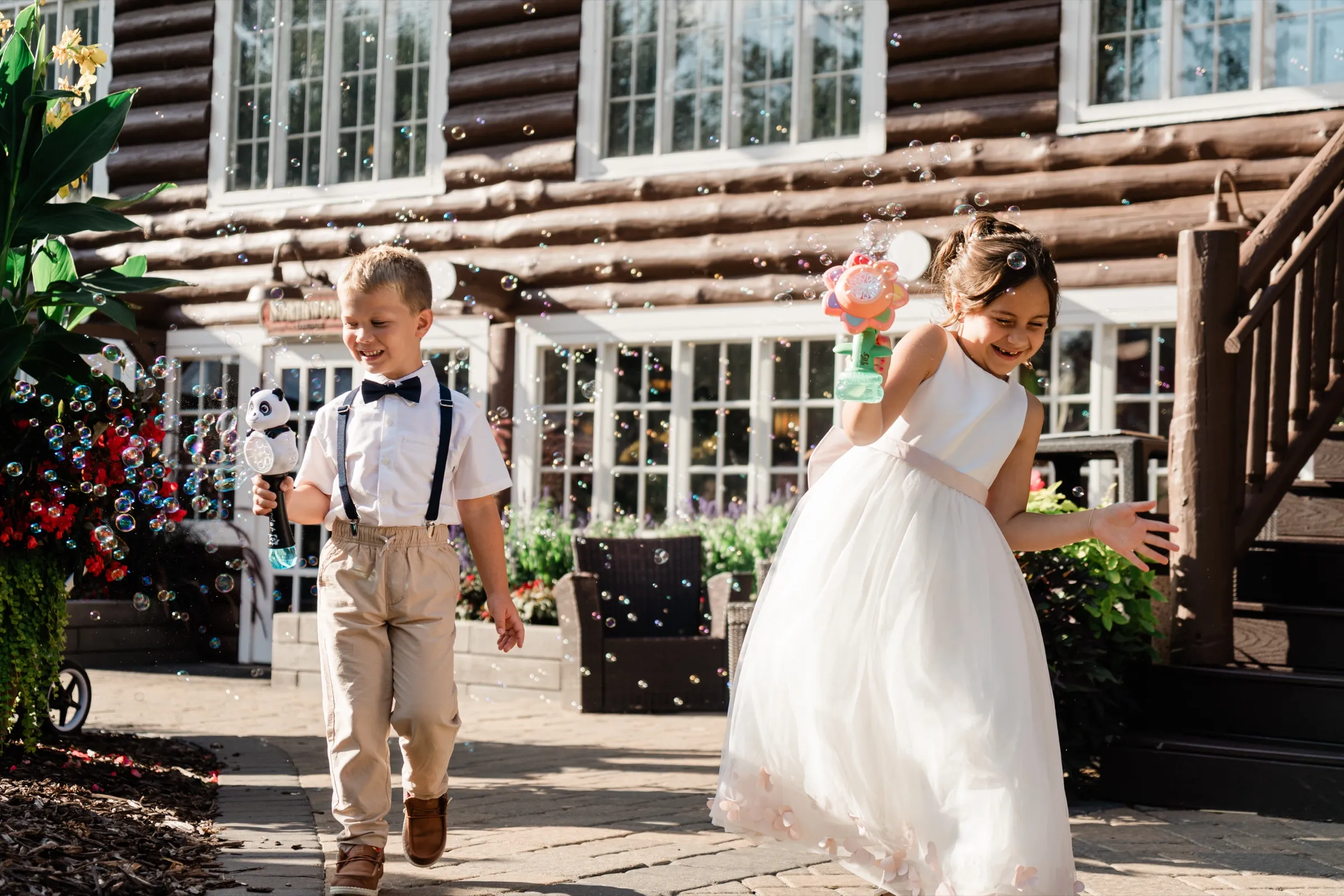 A flower girl and a ring bearer run past the log facade of the lodge firing bubble guns, with bubbles catching the low sun around them. — Tim Larsen Photography, Brainerd Lakes MN