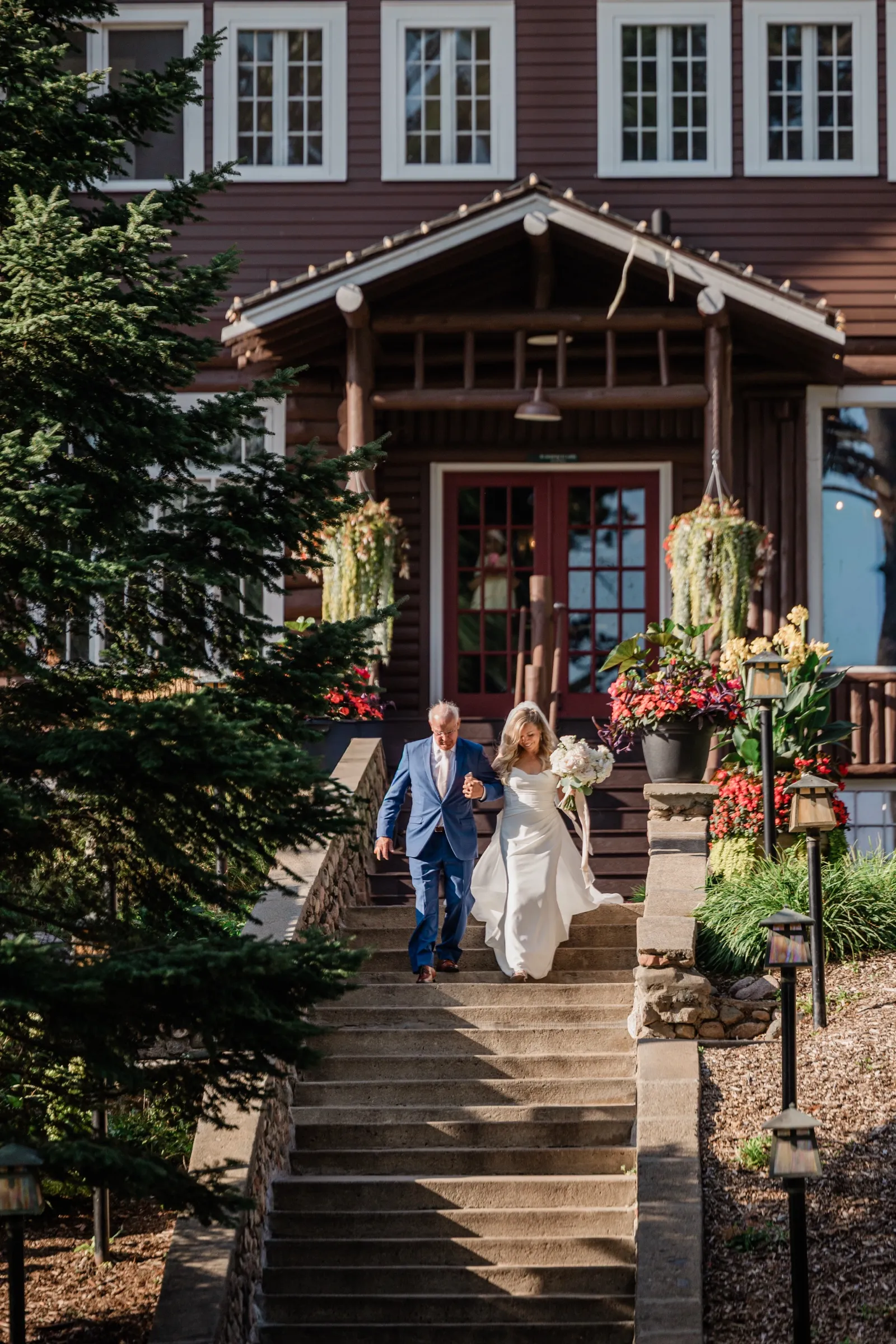 The bride and her father start down the wide stone staircase from the historic log lodge entrance, her gown catching the light behind her. — Tim Larsen Photography, Brainerd Lakes MN