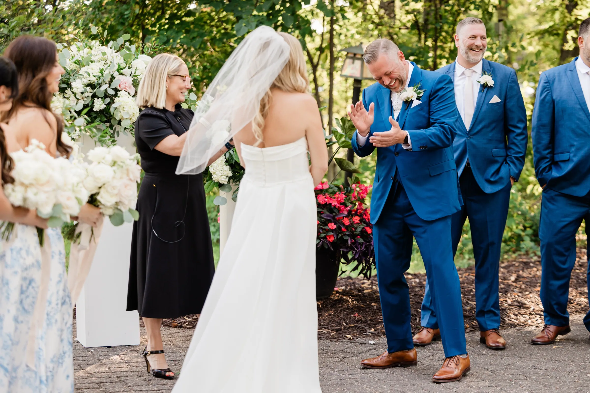 The groom laughs and claps his hands as the bride, seen from behind in her veil, arrives at the front of the ceremony. — Tim Larsen Photography, Brainerd Lakes MN