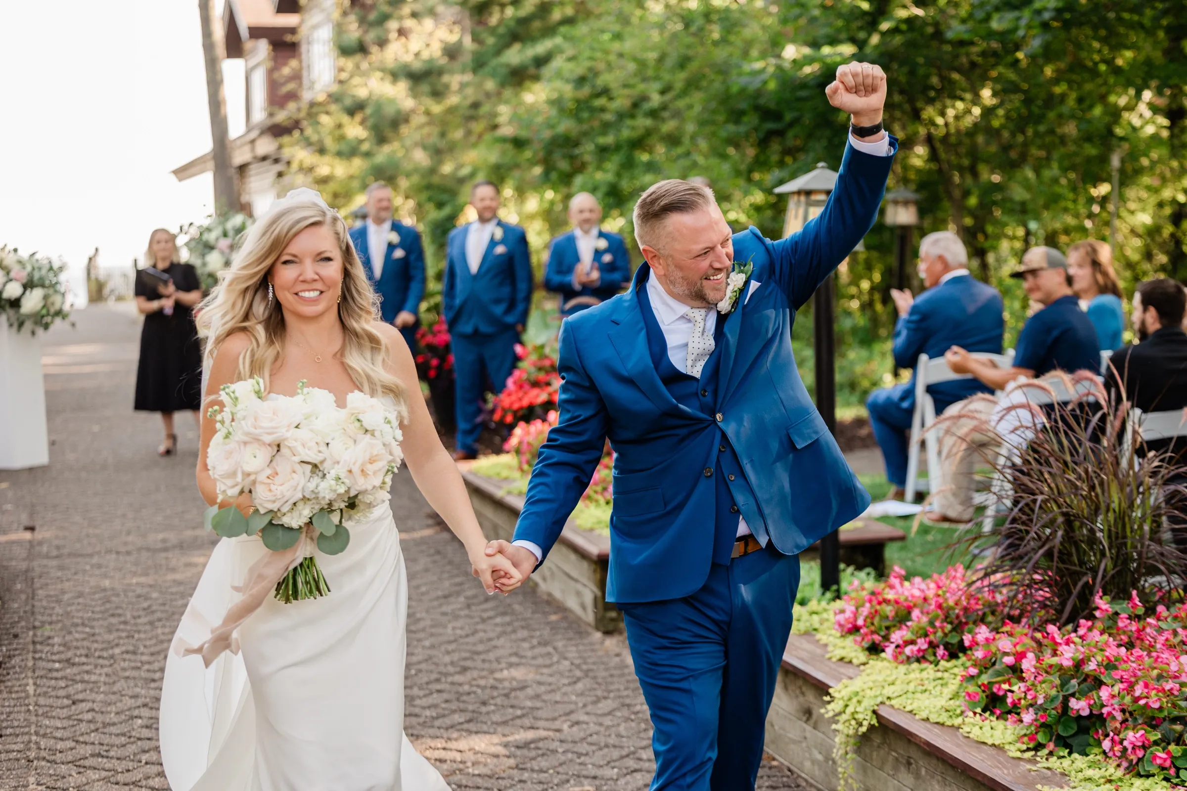 Walking back down the aisle hand in hand, the groom throws one fist in the air while the bride laughs beside him. — Tim Larsen Photography, Brainerd Lakes MN