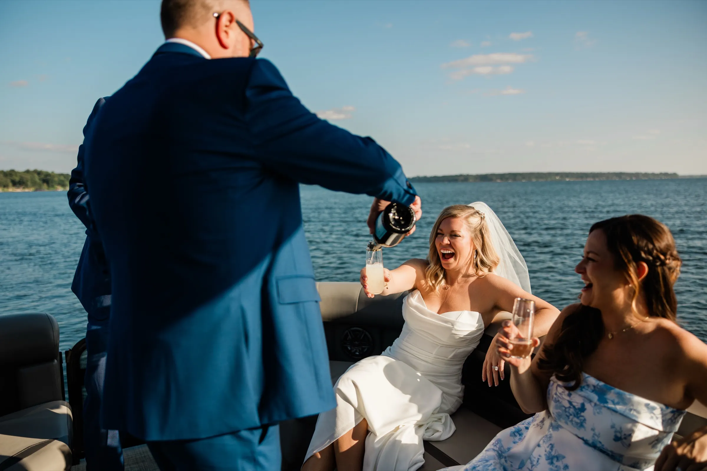 Seated on a pontoon boat with Gull Lake behind her, the bride laughs with her head back while the groom pours champagne into her glass. — Tim Larsen Photography, Brainerd Lakes MN