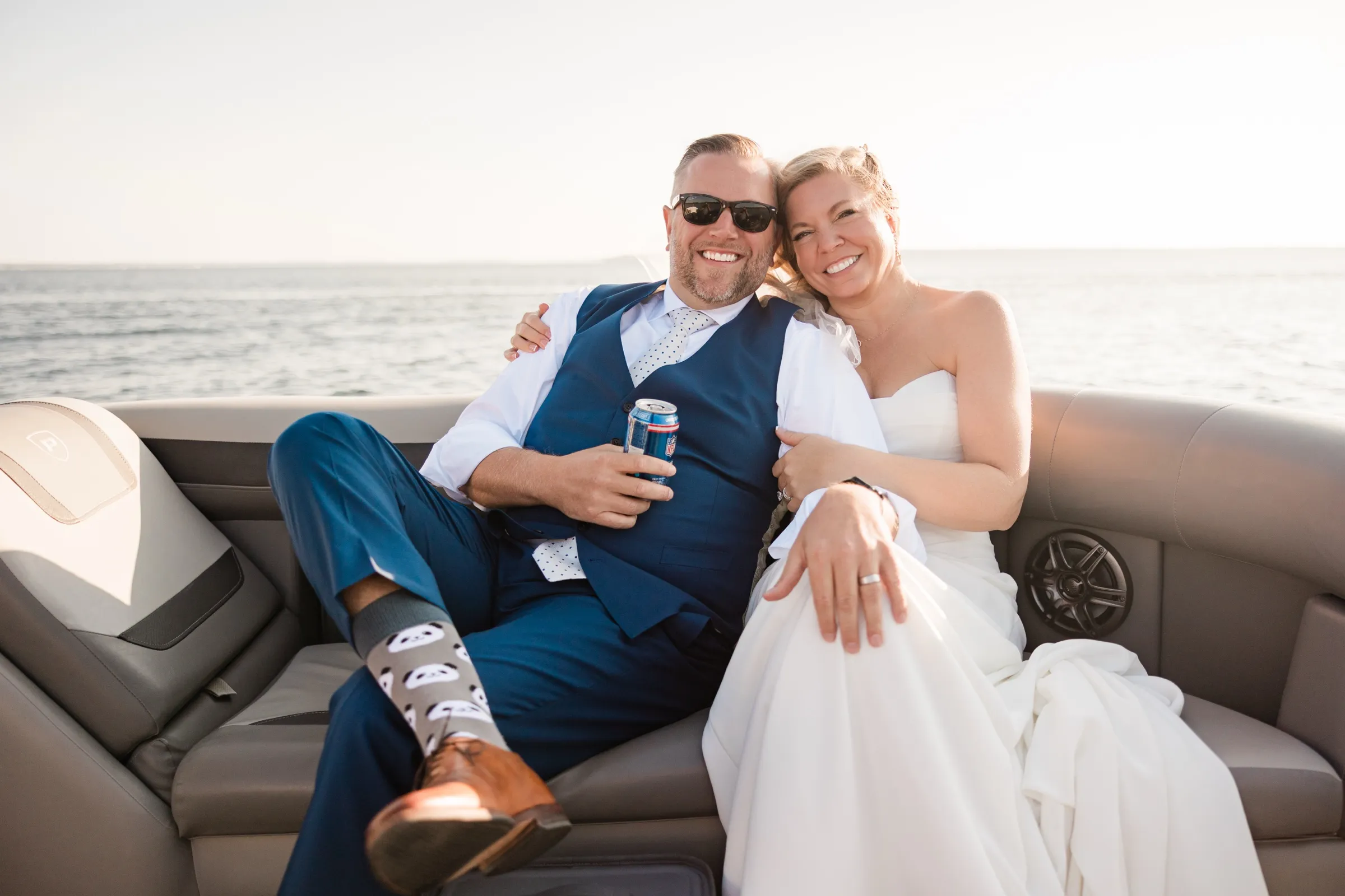 The bride and groom sit close together on a pontoon bench, his feet propped up, with the open lake behind them. — Tim Larsen Photography, Brainerd Lakes MN