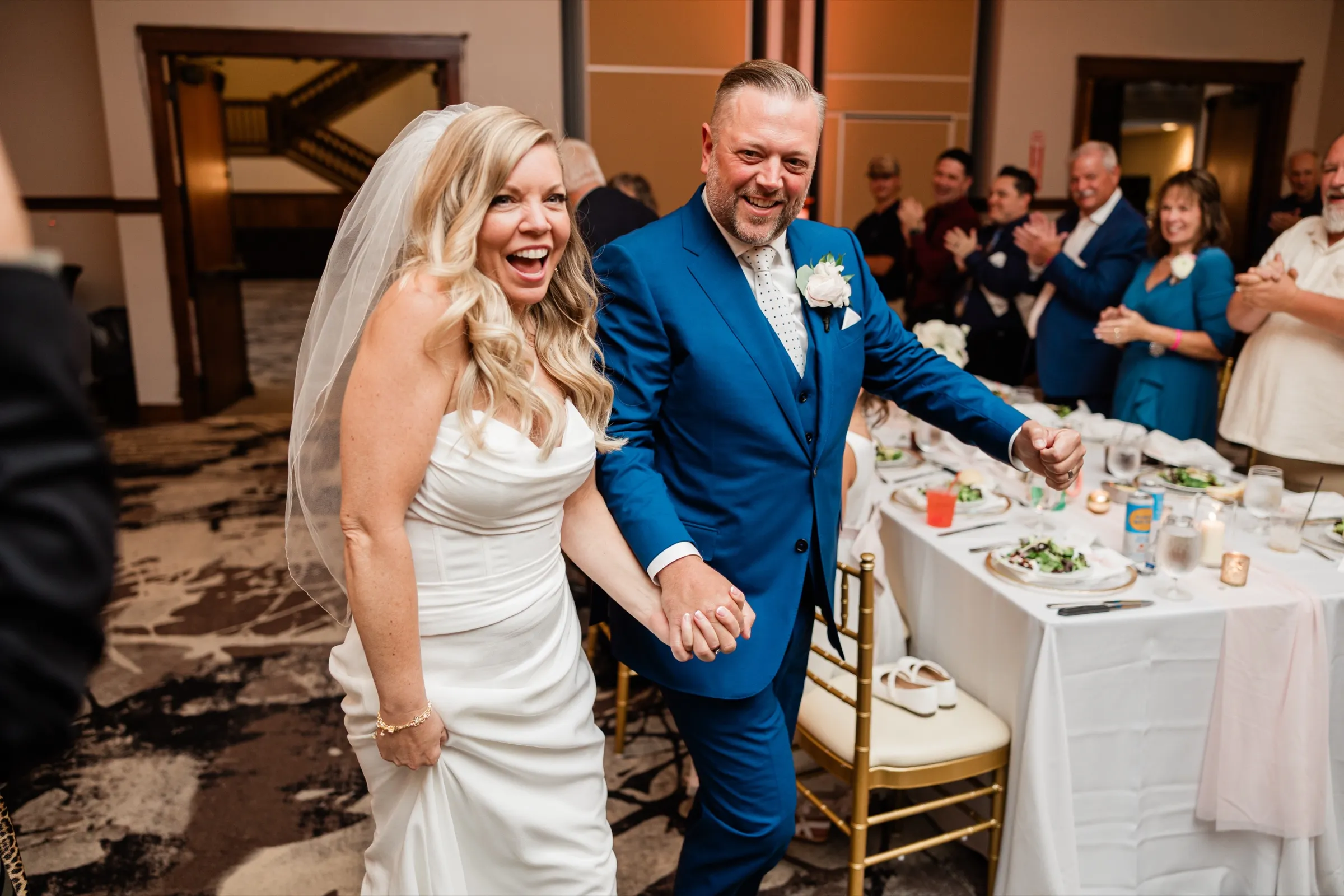 The bride and groom walk into the reception laughing, hands linked, while guests applaud behind the head table. — Tim Larsen Photography, Brainerd Lakes MN