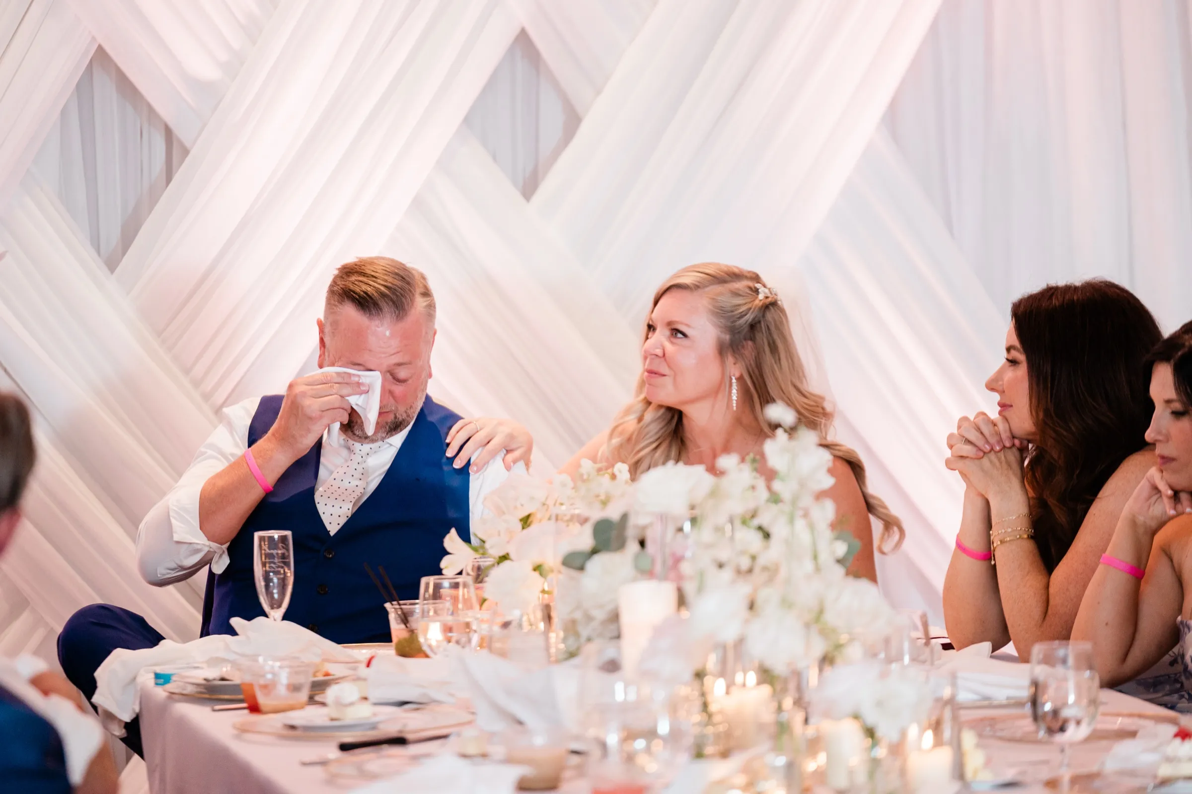 The groom listens during a toast at the head table while the bride rests her hand on his arm and watches him. — Tim Larsen Photography, Brainerd Lakes MN