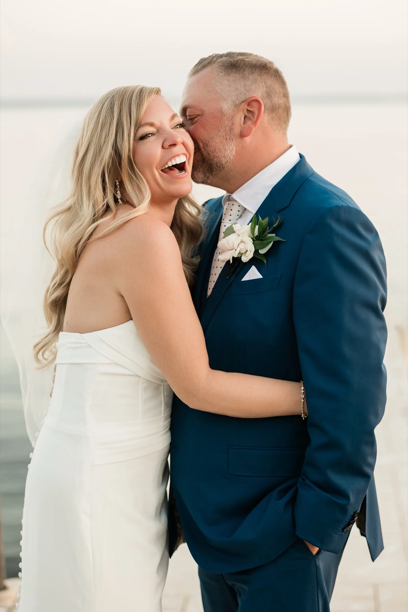 The bride laughs with her head tipped back while the groom kisses her on the cheek, close in frame on the dock. — Tim Larsen Photography, Brainerd Lakes MN