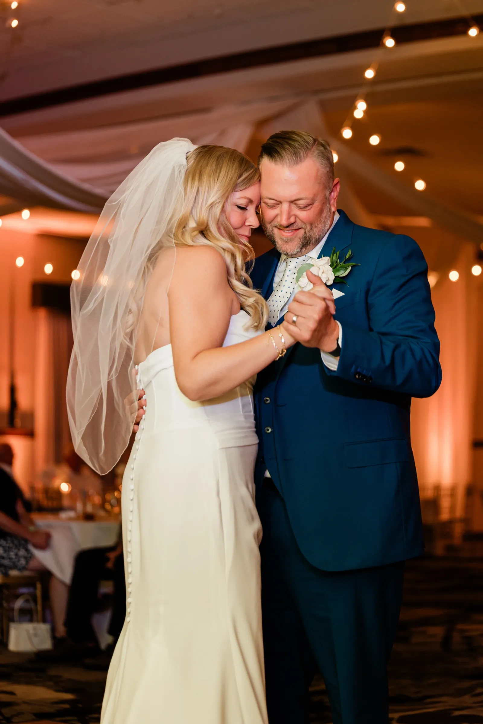 The bride and groom rest their heads together during the first dance, her veil lit by warm ambient light. — Tim Larsen Photography, Brainerd Lakes MN