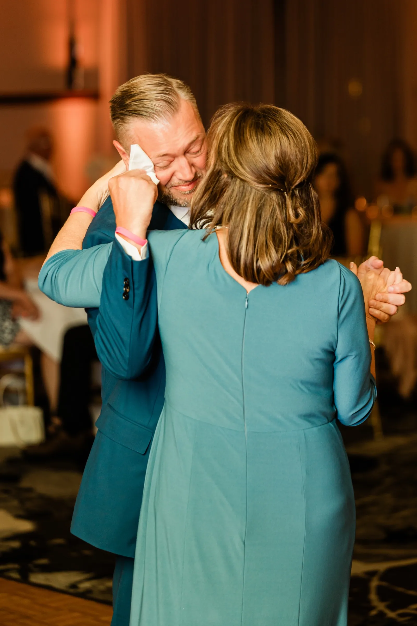 The groom dances with his mother, his head bowed toward her shoulder, under warm uplighting. — Tim Larsen Photography, Brainerd Lakes MN