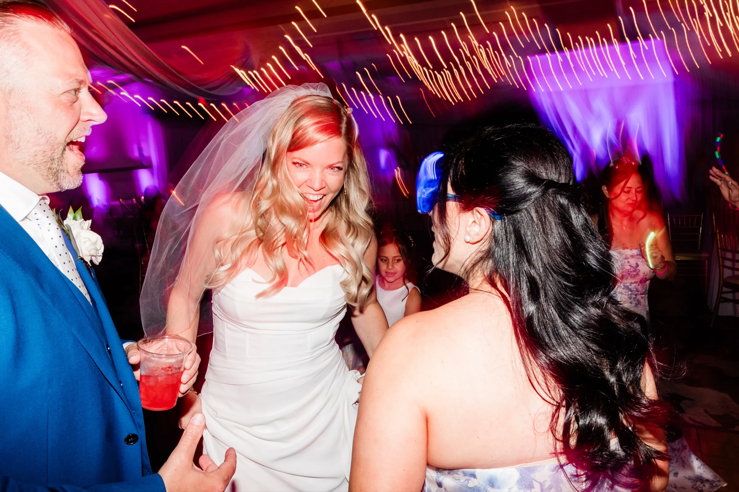 The bride shouts along with a song on a crowded dance floor while streaked light trails cut across the frame behind her. — Tim Larsen Photography, Brainerd Lakes MN
