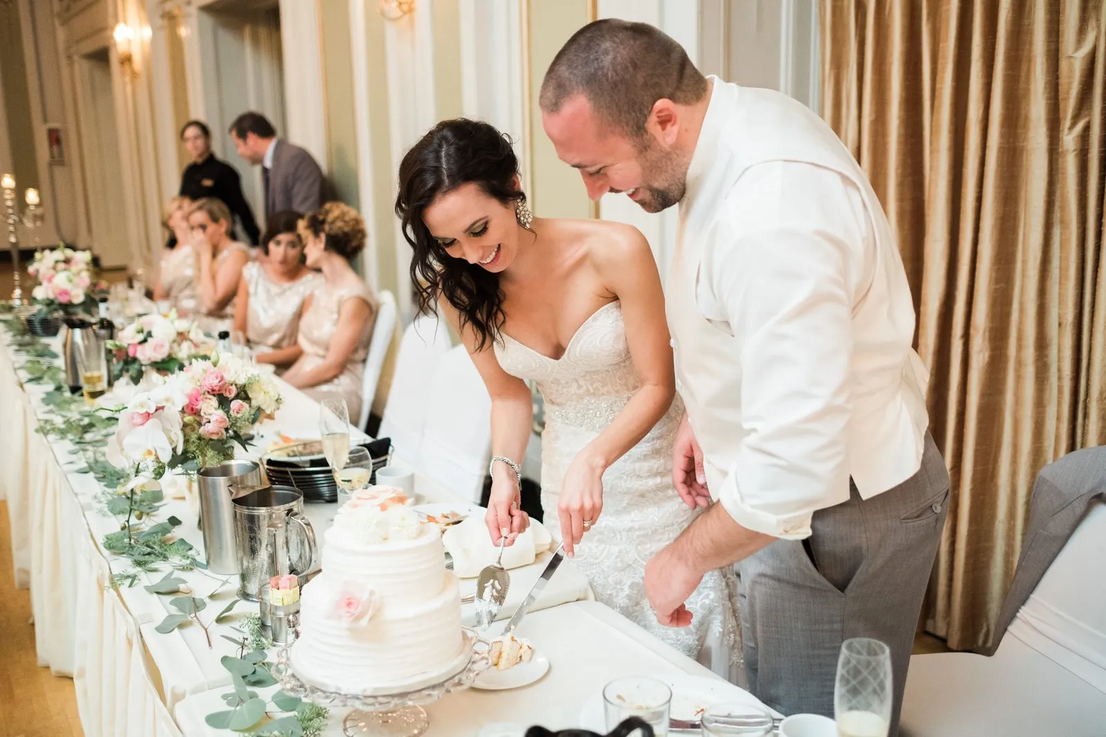Cake cutting at the head table — a strong foreground floral runner leads the eye to the couple mid-laugh at the Greysolon Ballroom reception — Tim Larsen Photography, Duluth MN