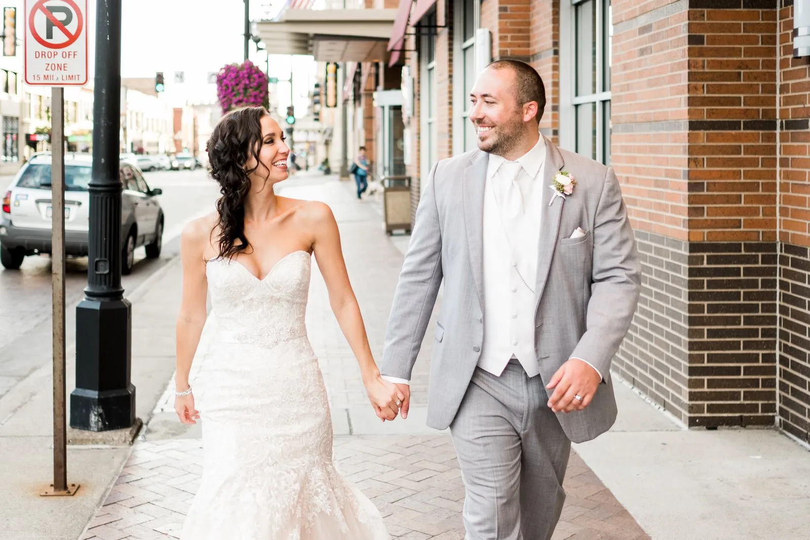 Couple walking hand-in-hand on a downtown Duluth brick sidewalk, exchanging a laughing glance against the historic urban backdrop — Tim Larsen Photography, Duluth MN