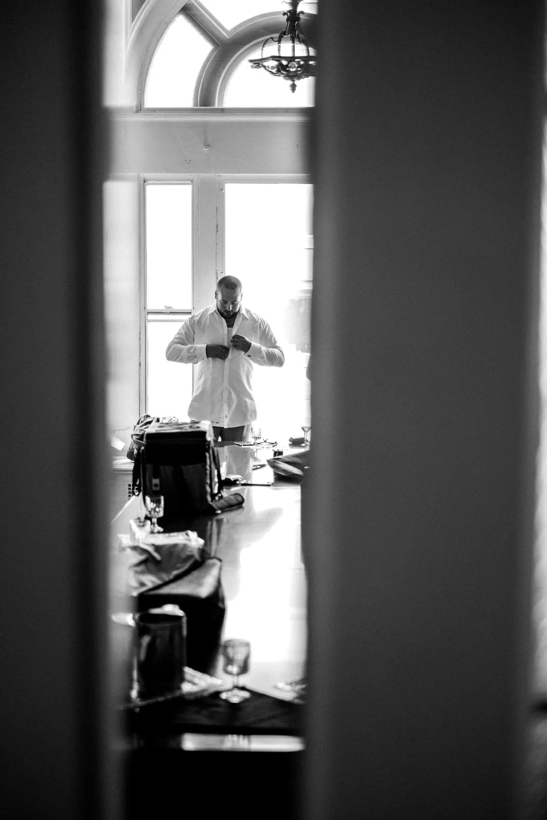 Doorway frames the groom backlit by a tall arched window in his Greysolon Plaza getting-ready room — autumn wedding morning — Tim Larsen Photography, Duluth MN