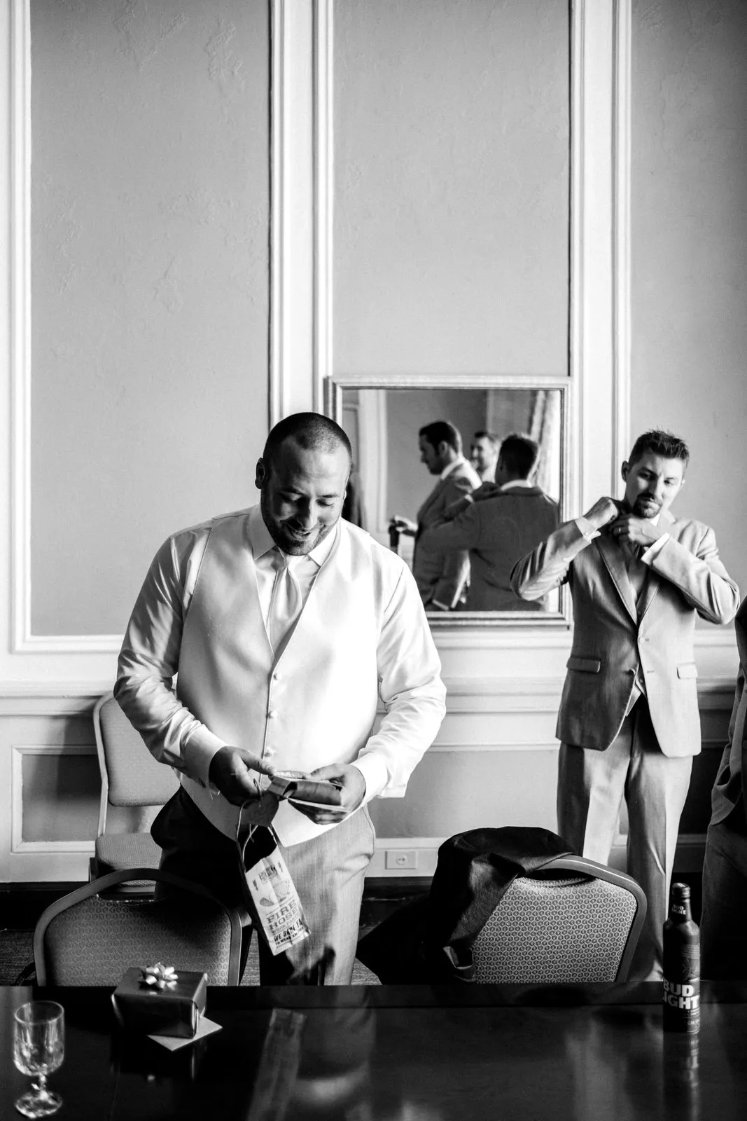 Groom in the foreground reading a gift tag while his groomsmen are reflected in the mirror behind — Greysolon Plaza getting-ready room — Tim Larsen Photography, Duluth MN