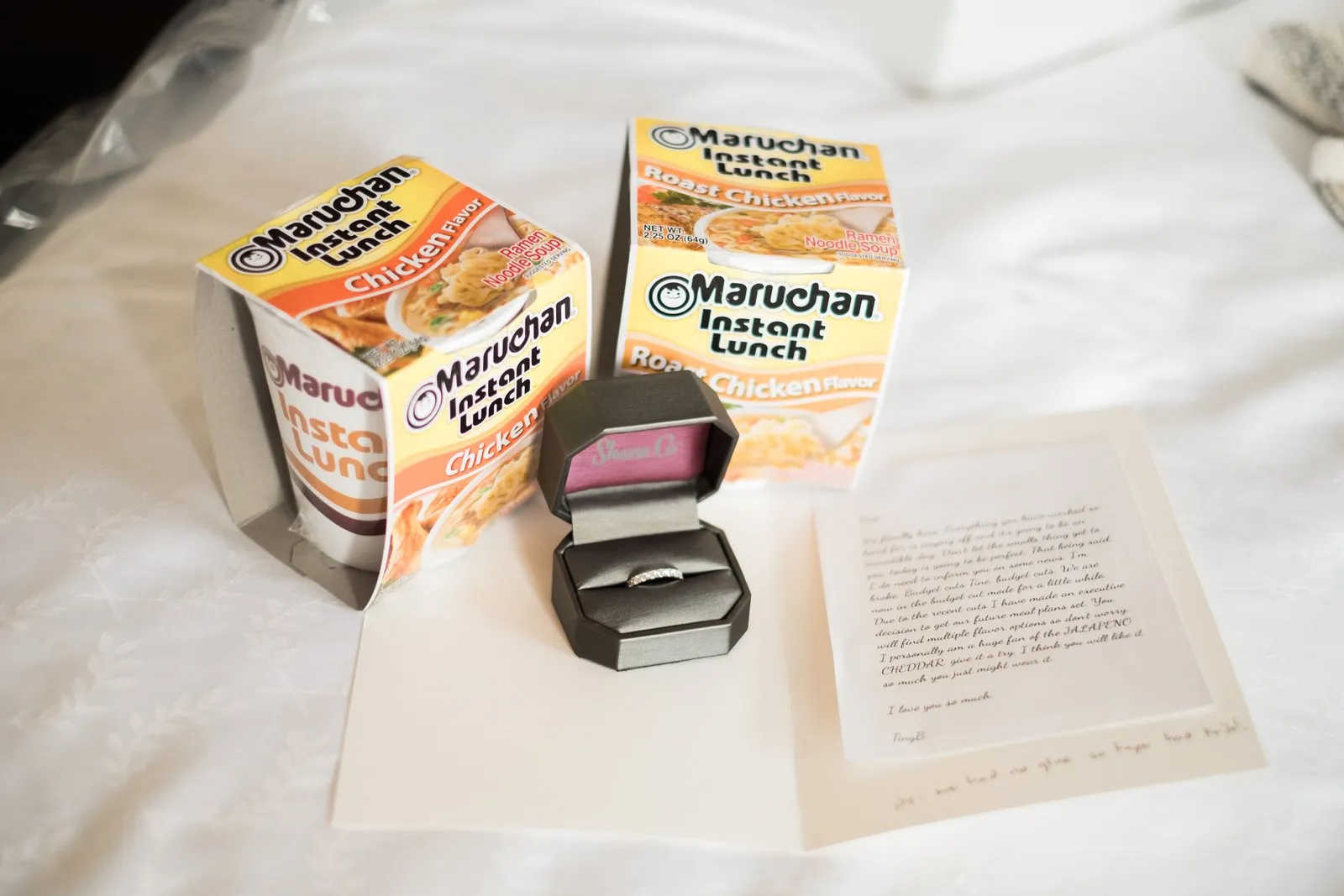 Detail shot — ramen cups flank a wedding ring box and a handwritten note staged on white bedding in the Greysolon bridal suite — Tim Larsen Photography, Duluth MN
