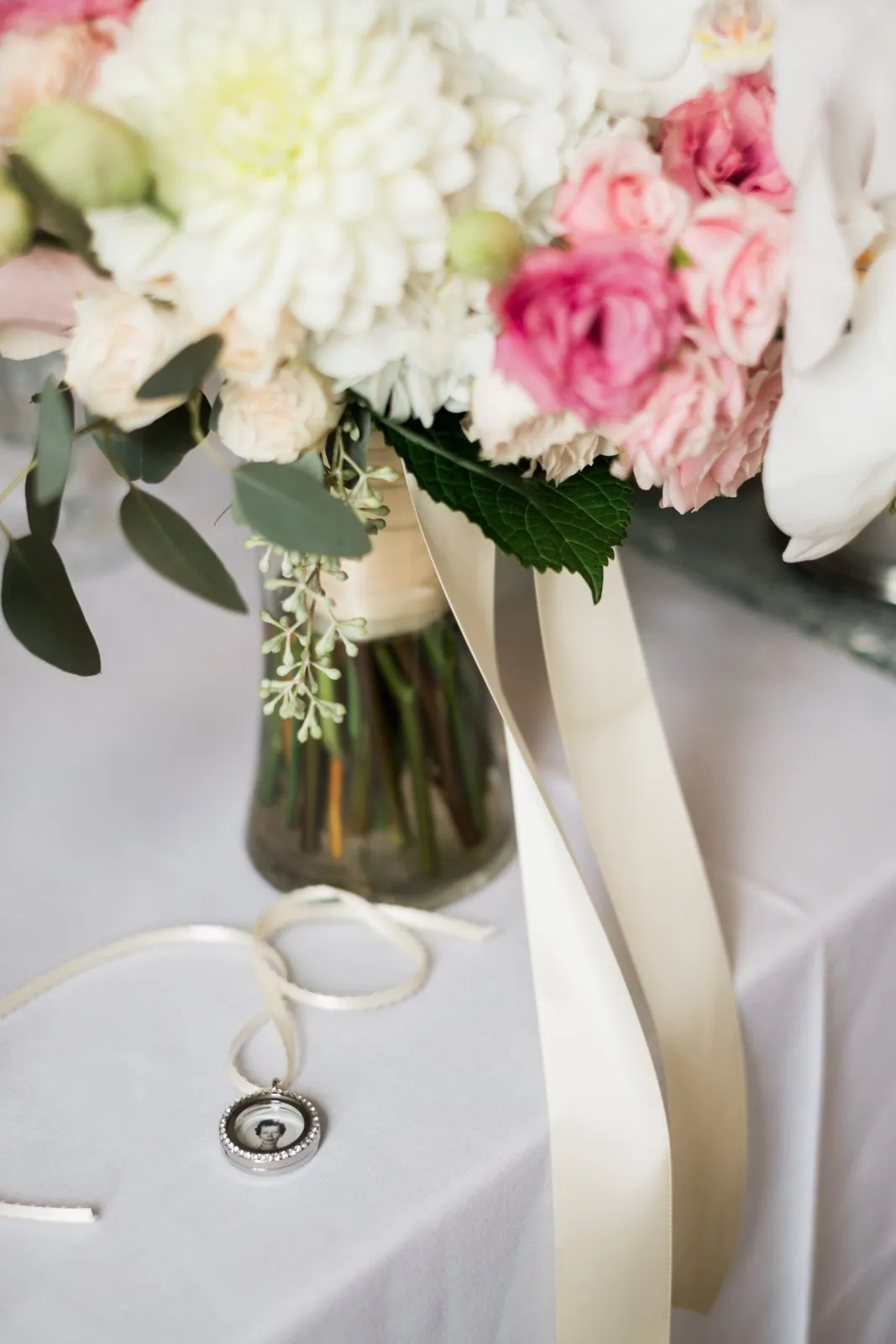 Coda detail — bridal bouquet above and a memorial locket with a photo and trailing ribbon below on the Greysolon reception table — Tim Larsen Photography, Duluth MN