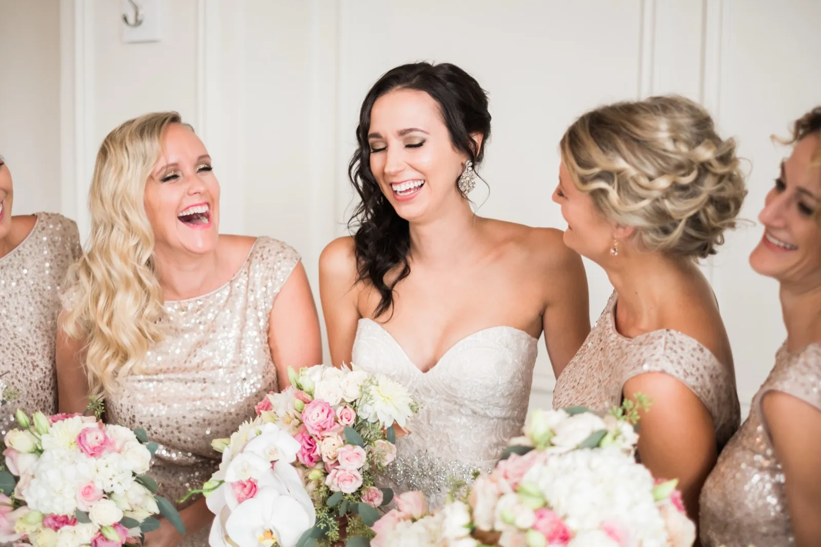 Bride centered between her laughing bridesmaids in champagne sequined dresses, cascading orchid bouquets framing the foreground at the Greysolon bridal suite — Tim Larsen Photography, Duluth MN