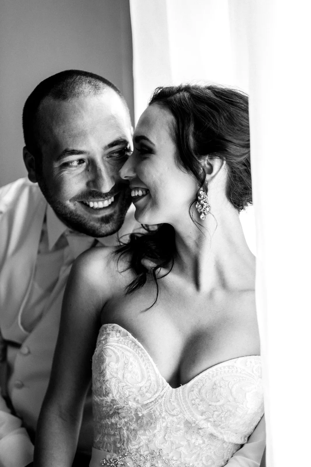 Black-and-white tight couples close-up against a bright Greysolon Plaza window, sheer curtain framing the right edge — intimate post-ceremony portrait — Tim Larsen Photography, Duluth MN