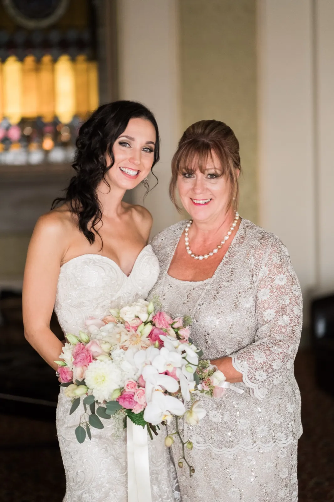 Family formal — bride and her mother centered with the warm glow of a stained-glass window behind them, bouquet anchoring the foreground at the Greysolon Ballroom — Tim Larsen Photography, Duluth MN