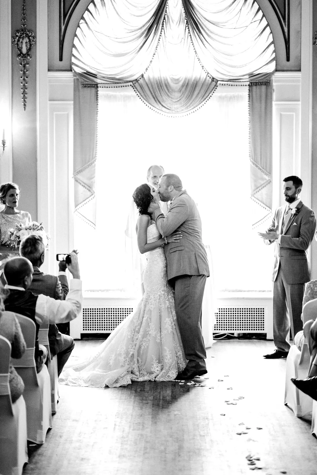 Backlit first kiss at the Greysolon Ballroom altar, framed by ornate draped windows along the symmetrical aisle — Tim Larsen Photography, Duluth MN