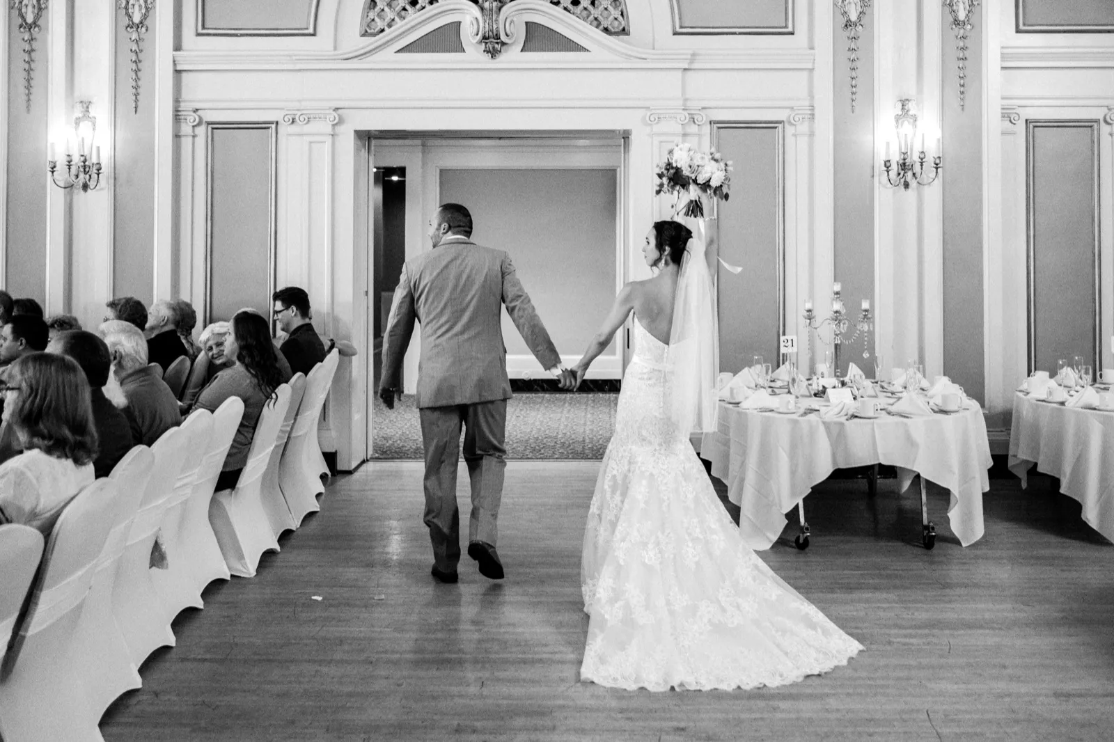 Bride and groom framed in an ornate Greysolon Ballroom doorway, the bridal train trailing behind and guests flanking the aisle — autumn wedding recessional — Tim Larsen Photography, Duluth MN