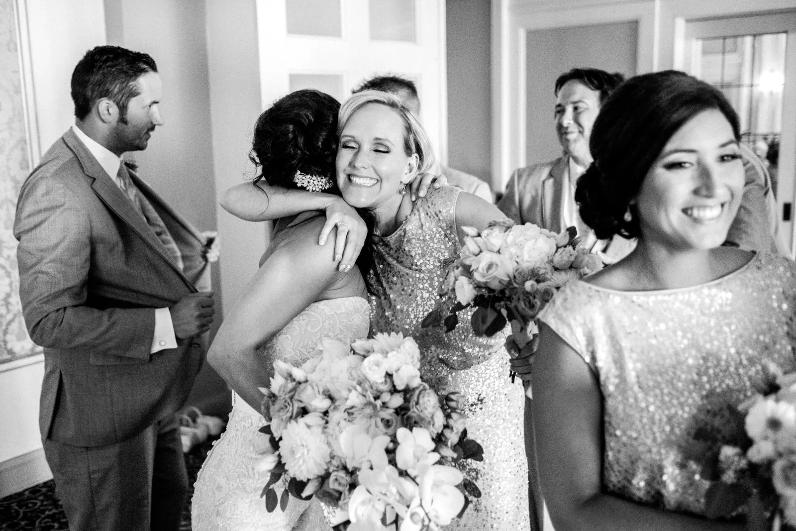 Bride’s beaming face framed by a tight hug just after the ceremony, layered figures and her bouquet anchoring the foreground at the Greysolon Plaza — Tim Larsen Photography, Duluth MN