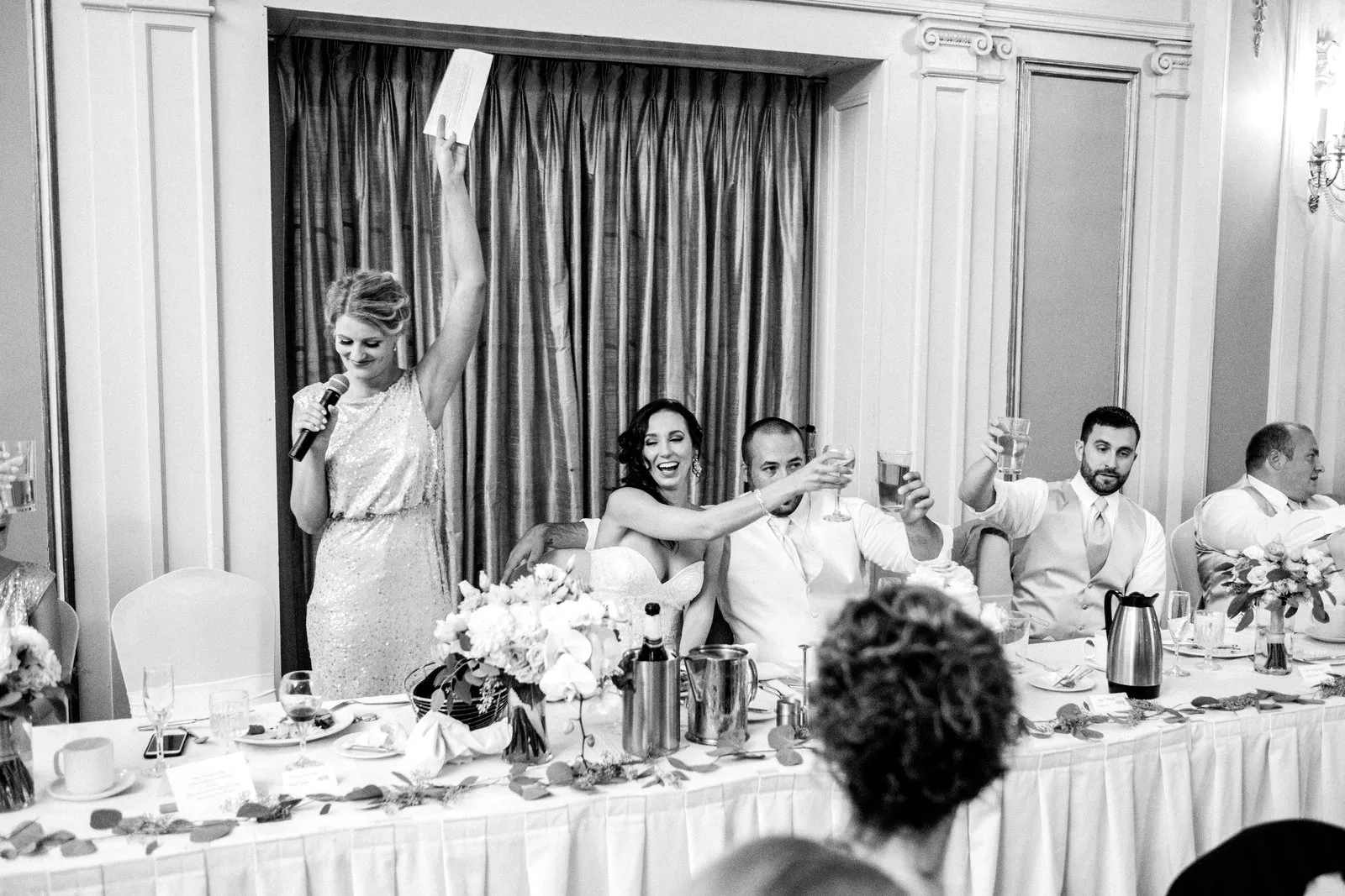Toasts at the head table — speaker’s raised arm anchors the left, the bride’s laugh and lifted glasses cascading right at the Greysolon Ballroom reception — Tim Larsen Photography, Duluth MN