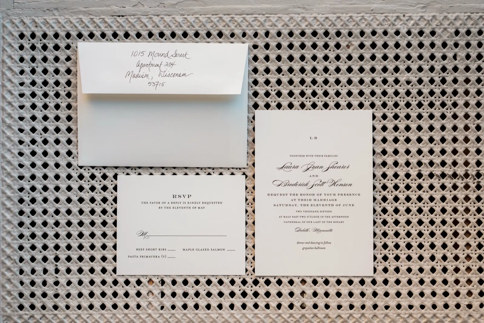 The Larsen letterpress wedding invitation suite — handwritten envelope, RSVP card, and main invite arranged on a textured woven cane background — Tim Larsen Photography, Duluth MN